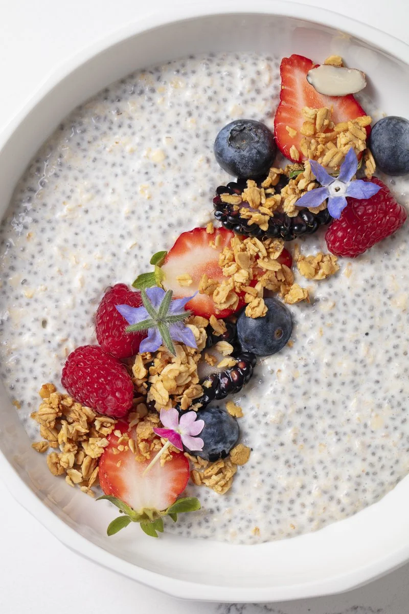 A bowl of chia seed pudding topped with strawberries, blueberries, blackberries, granola, edible flowers, and an almond slice.