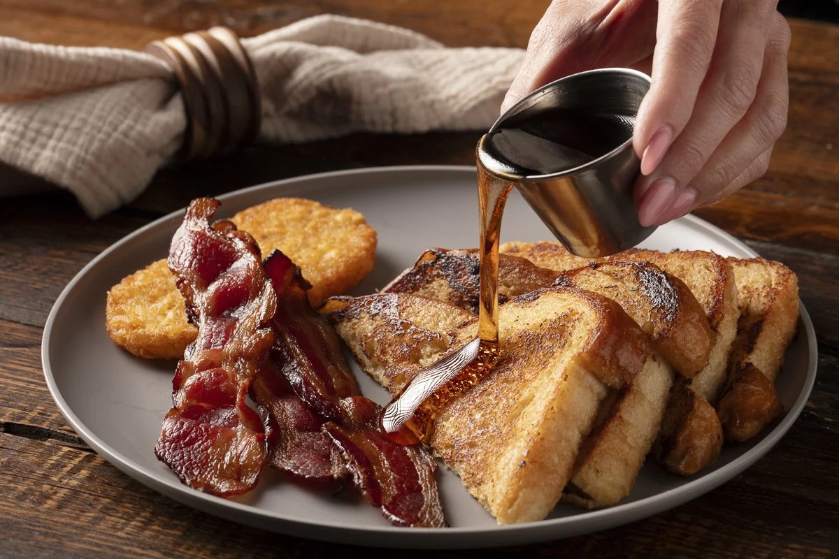 Hands reaching for French toast and bacon at a brunch table - food lifestyle photographer, Orange County