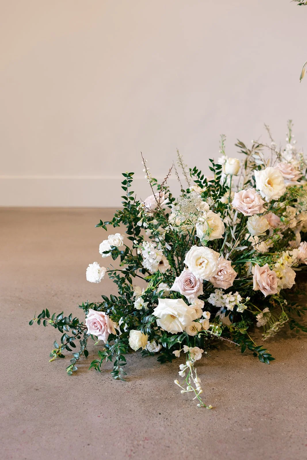 Lush ceremony installation featuring garden urns and meadows with petal heavy roses butterfly ranunculus, delphinium, and Queen Anne’s lace with natural, untamed greenery. Floral hues of white, cream, and blush. Designed by Rosemary and Finch in Nash