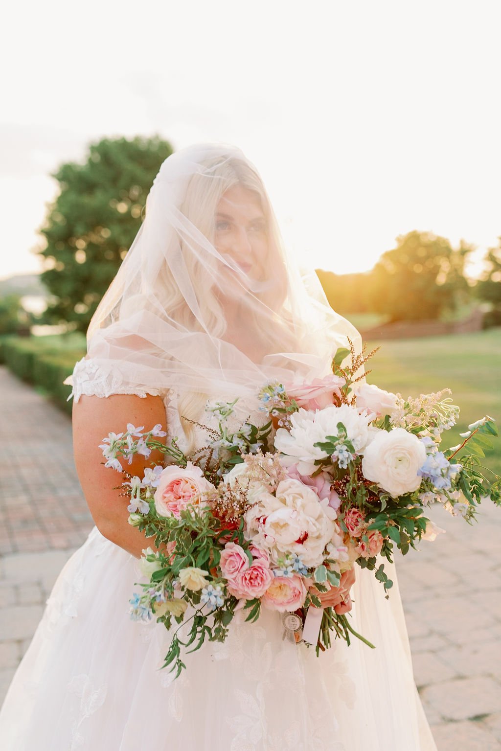 A lush bridal bouquet filled with hues of blush, pink, ivory, and hints of French blue. Garden roses, majolica spray roses, champagne roses, peonies, ranunculus, delphinium, and spirea make up this fairytale bouquet. Designed by Rosemary & Finch in N