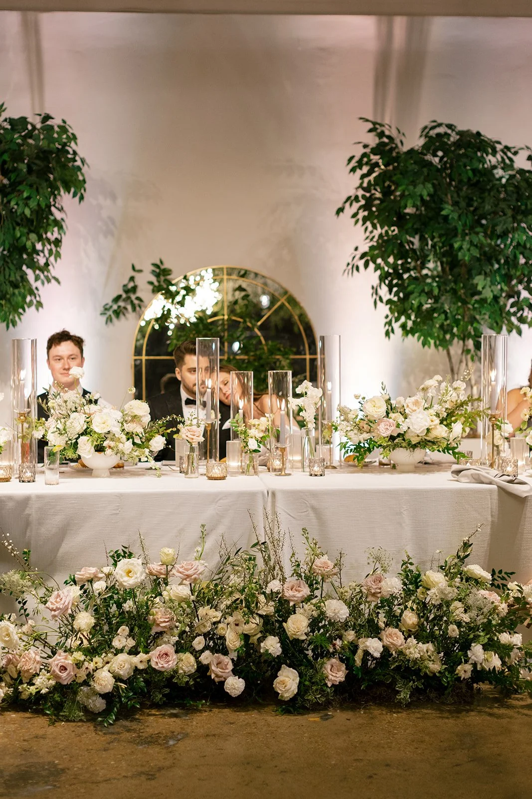 Low floral centerpieces for elegant wedding overflowing with white garden roses, ranunculus, butterfly ranunculus, scabiosa, lisianthus, sweet peas, and natural dark greenery. Floral hues of white, cream, and blush. Designed by Rosemary and Finch in