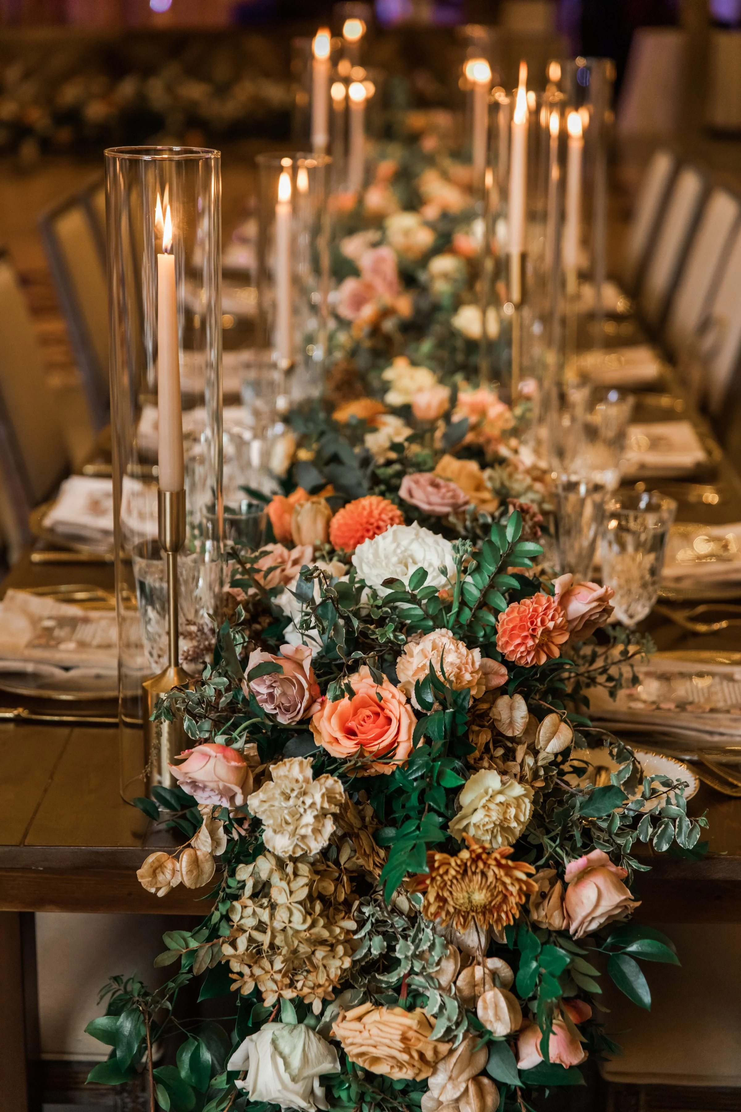 Stunning floral cascades line tables of this fall reception with terra cotta, blush, yellow hues, and taupe taper candles. Florals featuring dahlias, roses, and rain tree pods create lush arrangements. Designed by Rosemary and Finch in Nashville, TN.