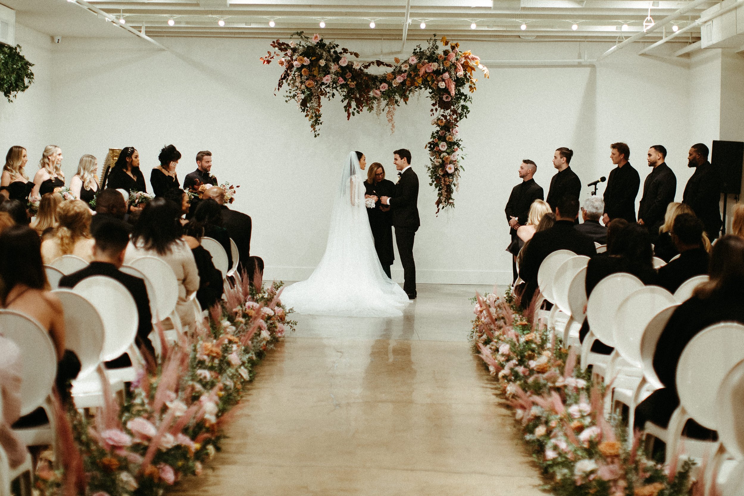 An eye-catching whimsical installation full of petal heavy roses and copper beech was the highlight of this art deco wedding. Terra cotta, burgundy, dusty pink, and other neutral florals warm up this ceremony. Designed by Rosemary and Finch in Nashvi