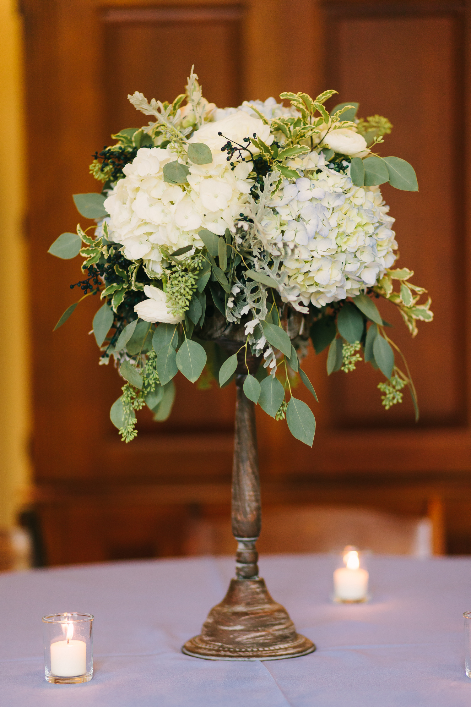 Elevated floral arrangement with blue and white hydrangeas, privet berries, and lush greenery