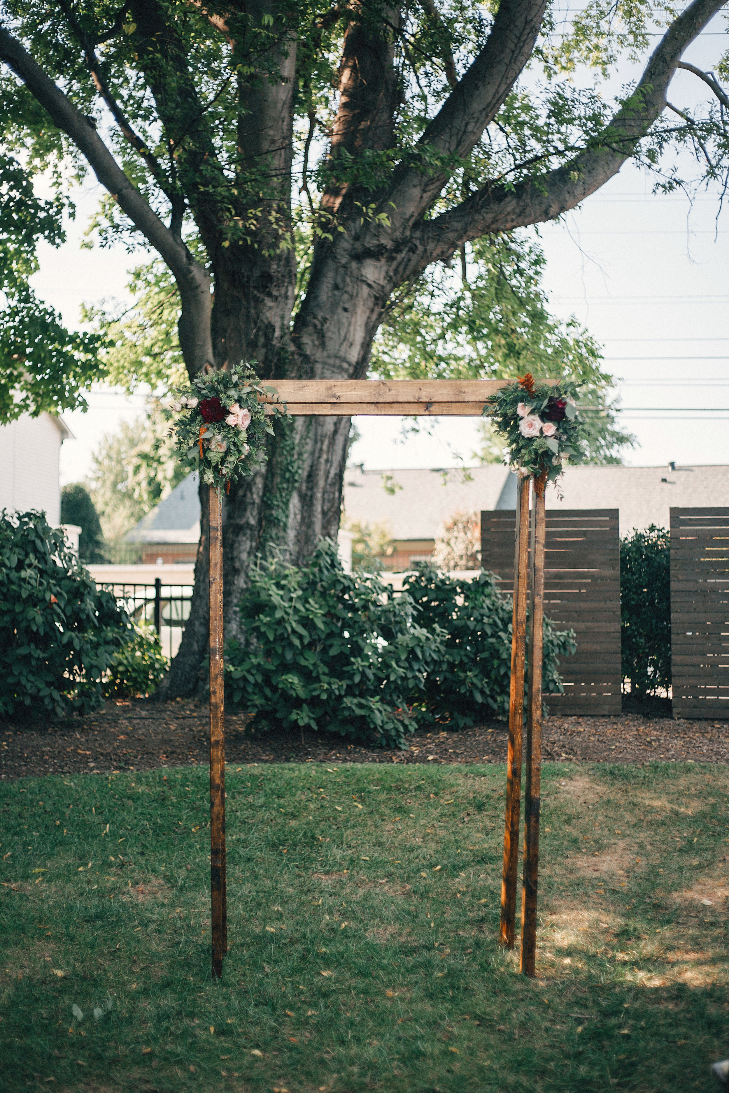 Simple wooden chuppah with burgundy, peach, gold, and greenery florals // Nashville Wedding Florist