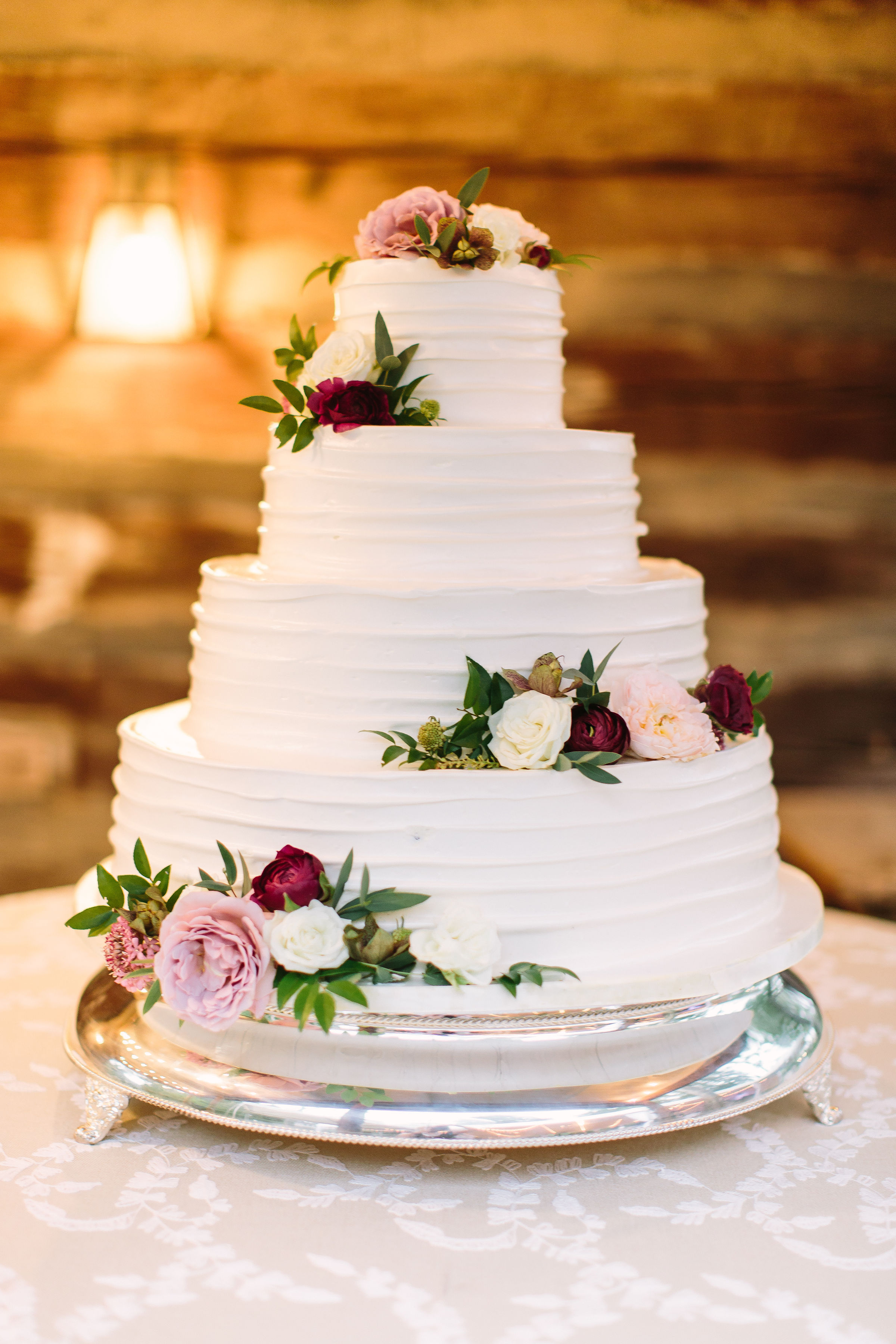 White, 4-tired wedding cake with clustered floral accents using garden roses, ranunculus, hellebores, and greenery // Nashville Wedding Floral Design