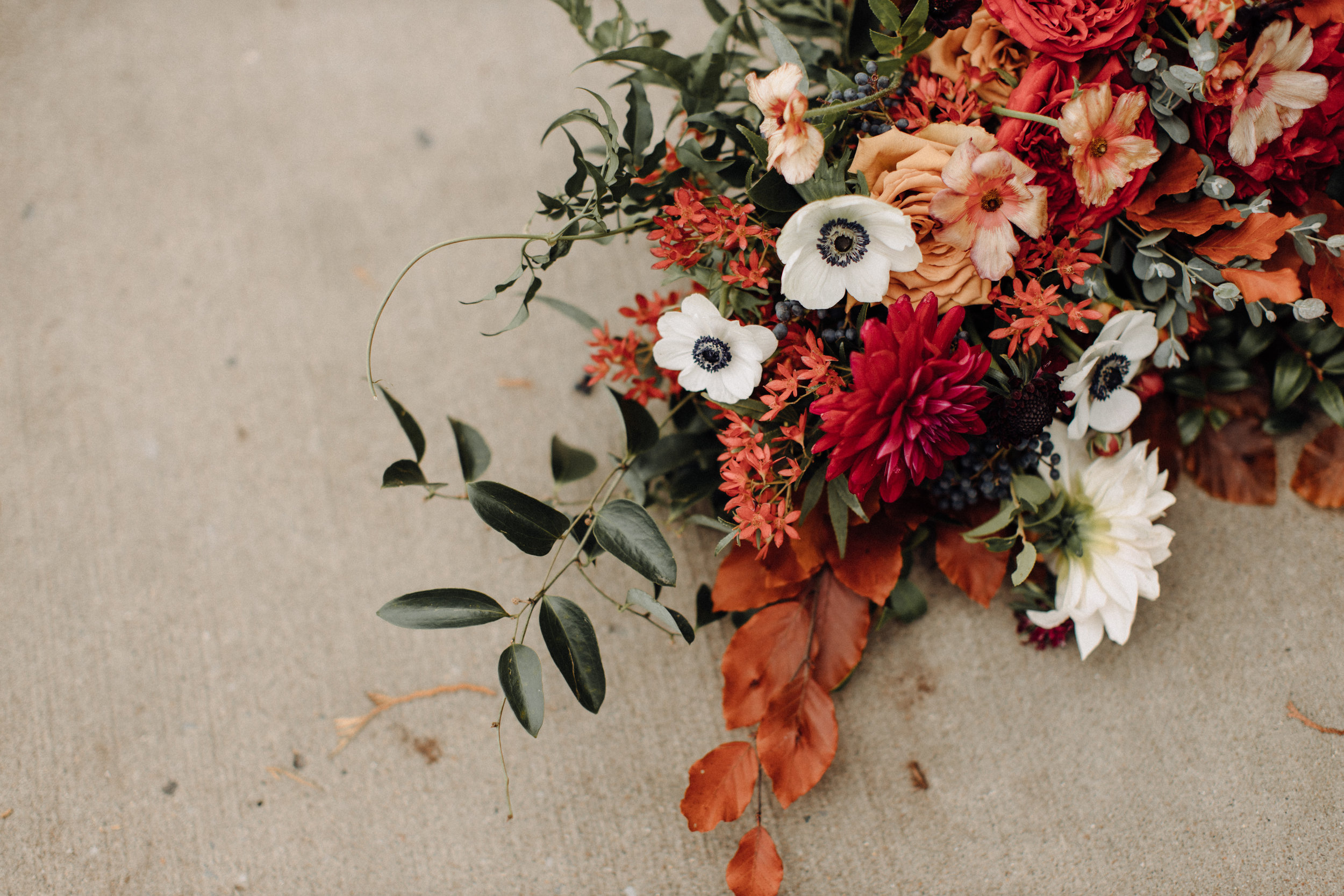 Asymmetrical, airy bridal bouquet with burgundy, burnt orange, and gold hues, using anemones, dahlias, and garden roses. Nashville, TN wedding florist.