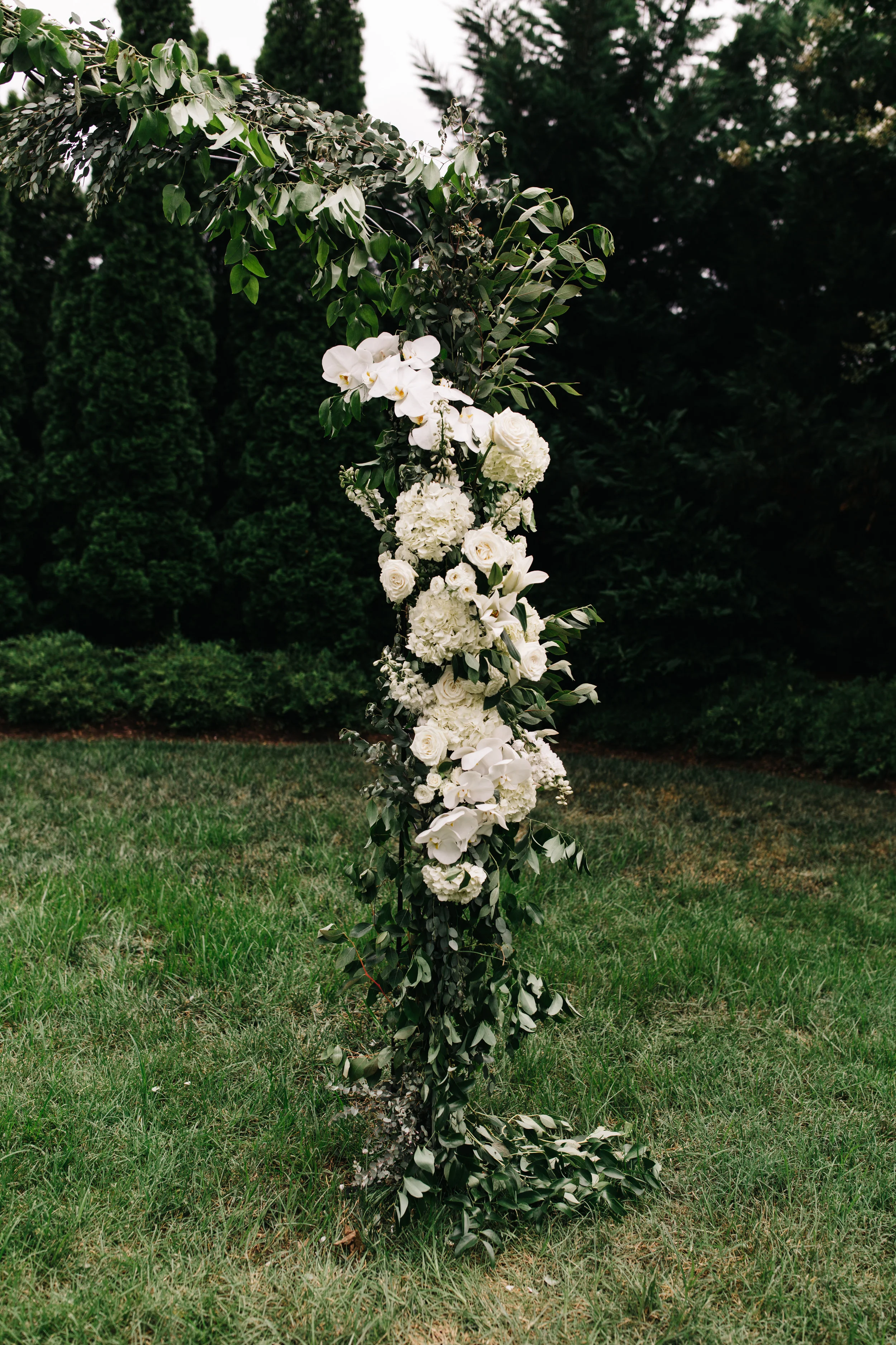 Lush garden arch for the ceremony backdrop with all white orchids, garden roses, and ranunculus. Southeastern US floral design for weddings.