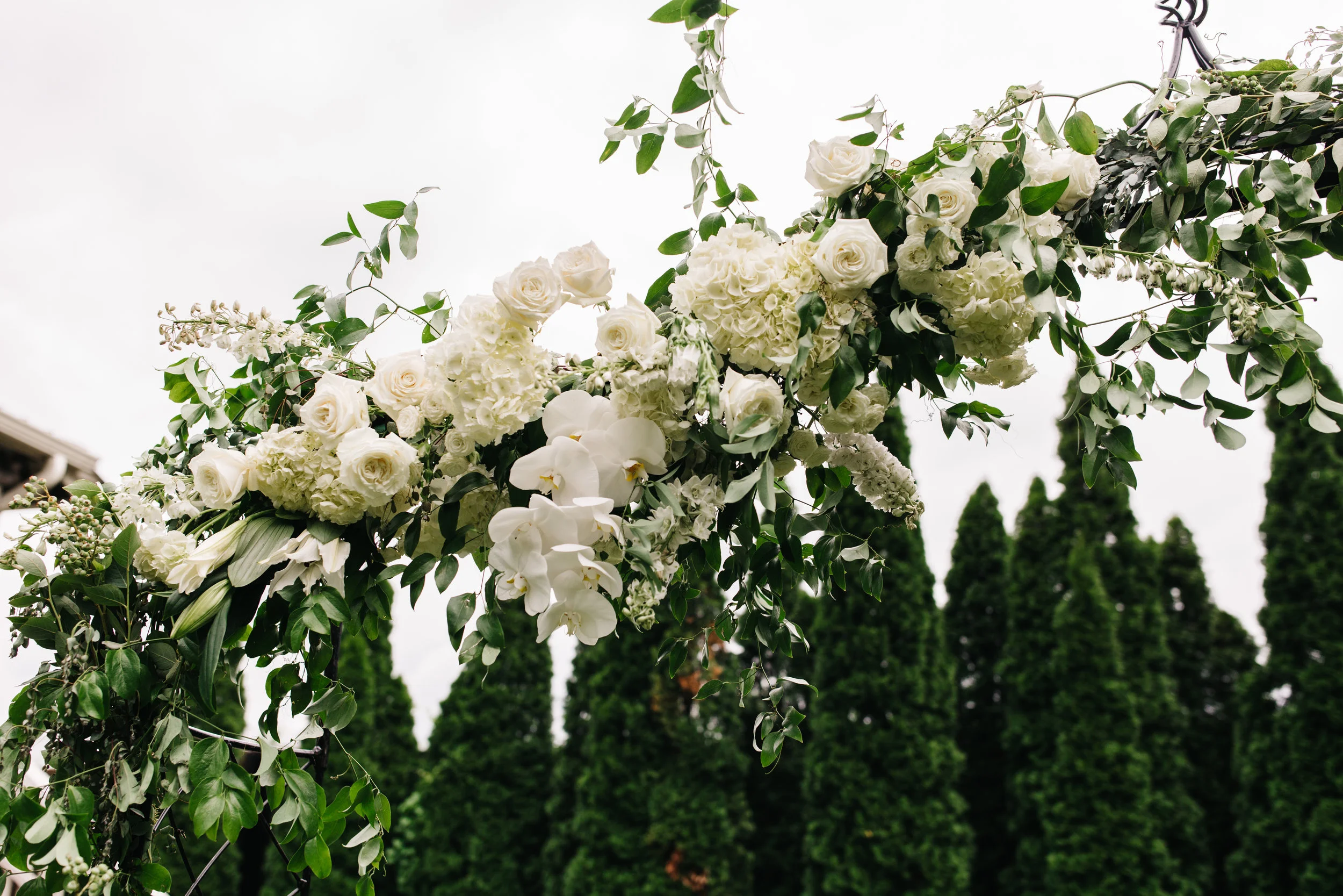 Lush garden arch for the ceremony backdrop with all white orchids, garden roses, and ranunculus. Southeastern US floral design for weddings.