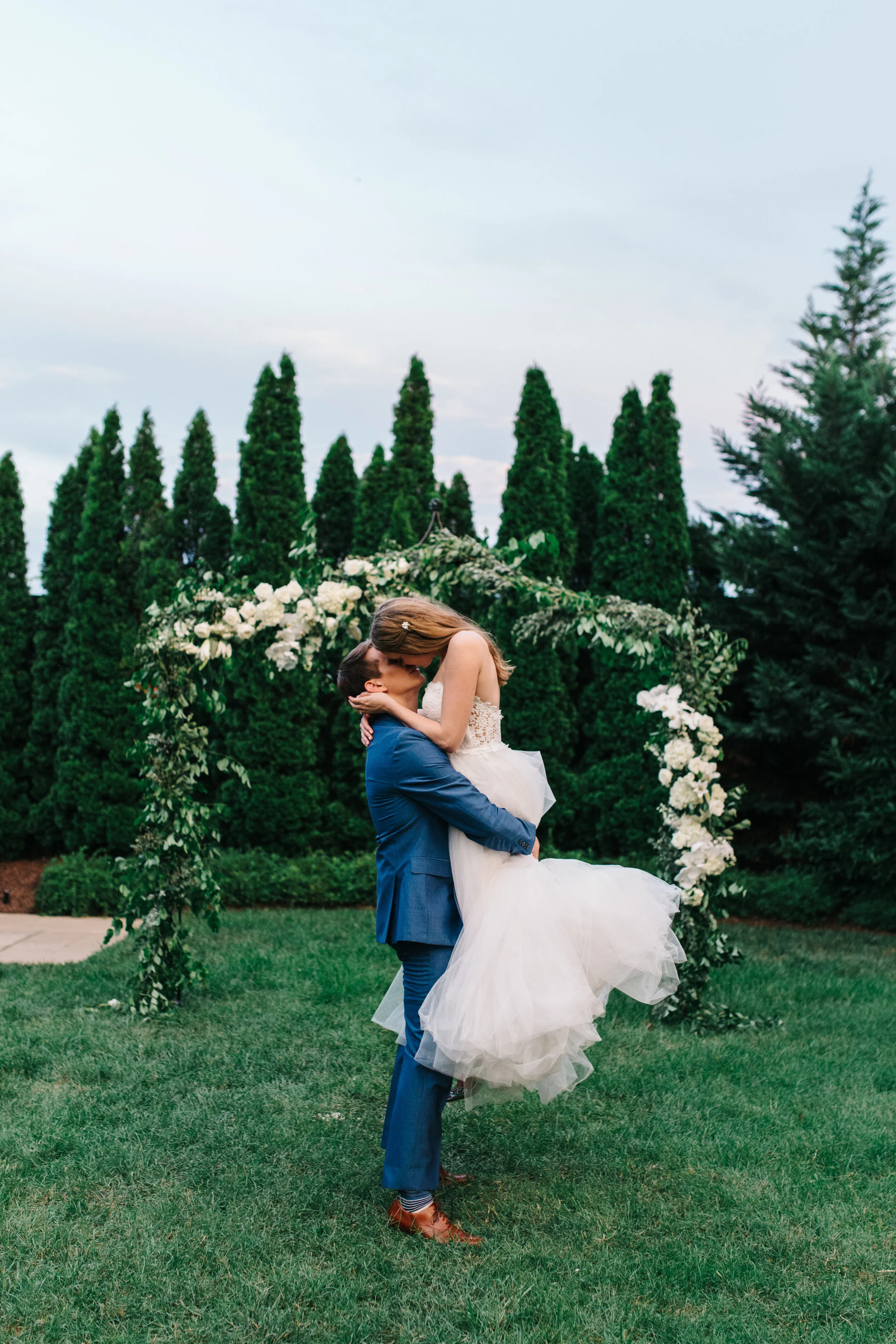 Lush garden arch for the ceremony backdrop with all white orchids, garden roses, and ranunculus. Southeastern US floral design for weddings.