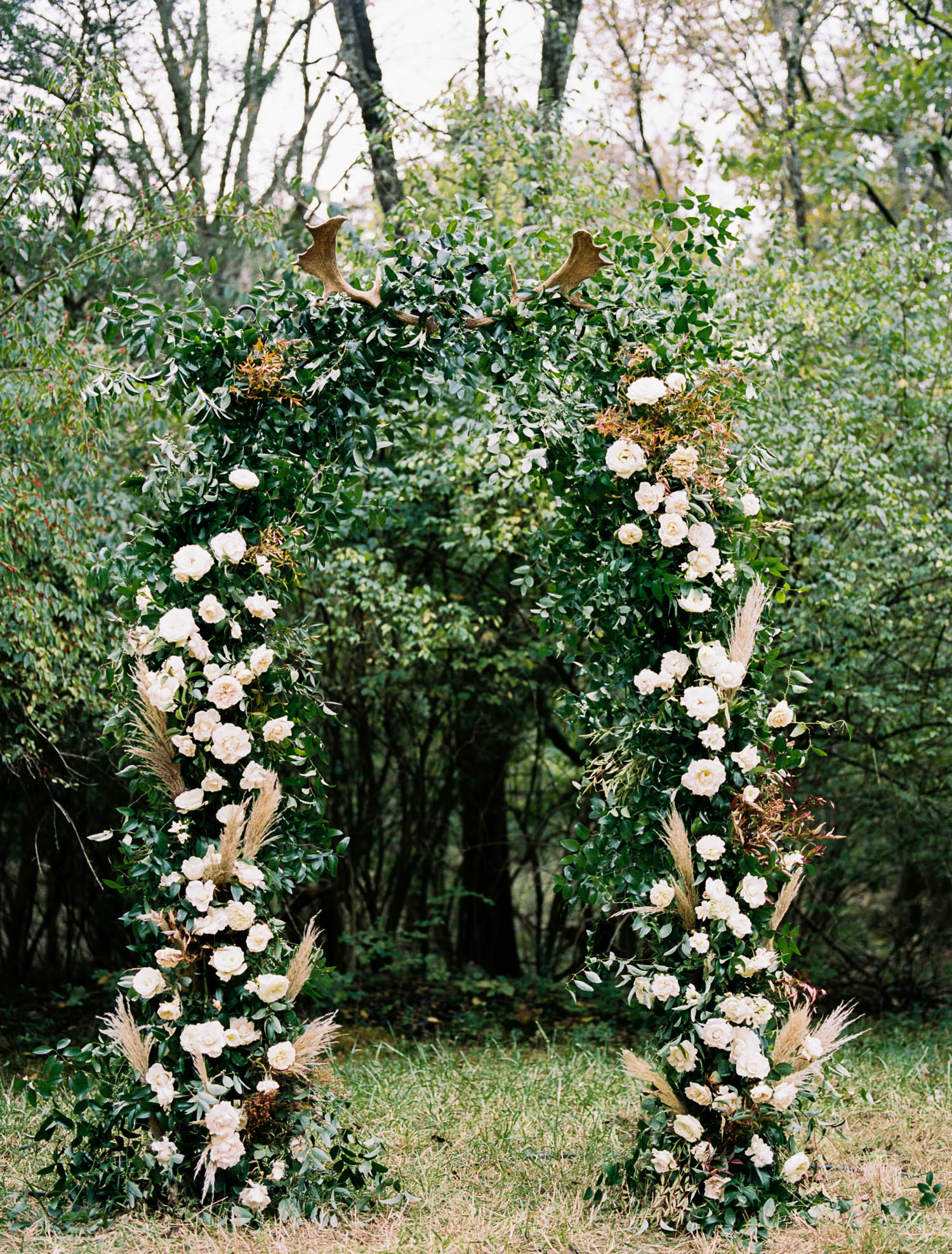 Lush wedding arch with untamed greenery, garden roses, textures, and antlers. Nashville Wedding Florist.