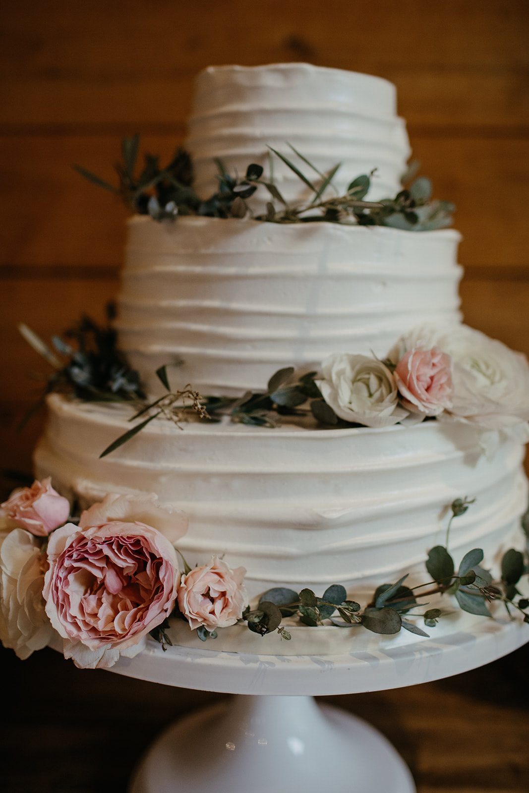 Wedding cake with eucalyptus wreaths and blush and peach garden roses and ranunculus. Nashville Wedding Floral Design.