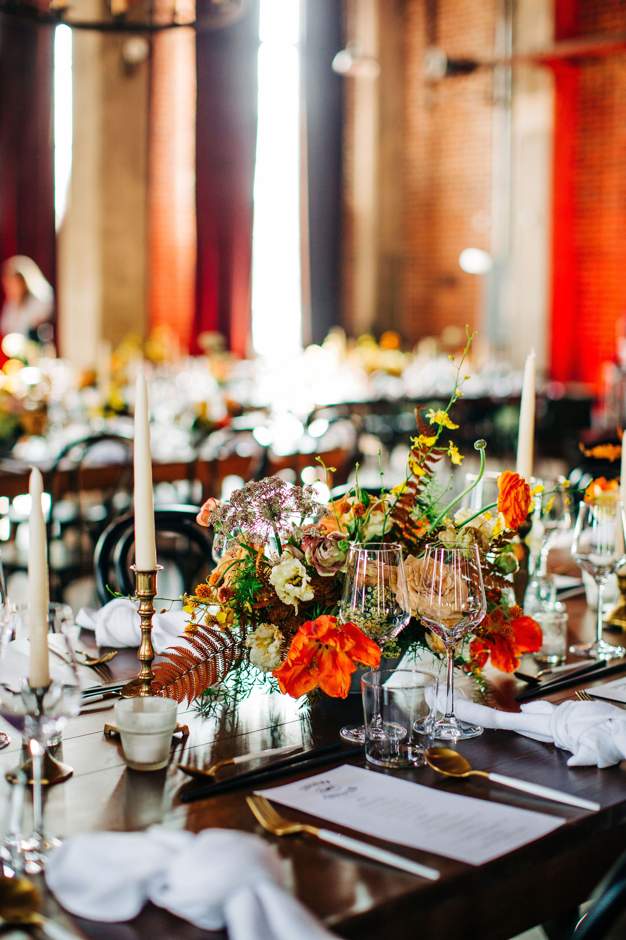 Yellow peonies, orange ranunculus, and golden fern floral centerpieces with brass candlesticks. Nashville wedding florist.