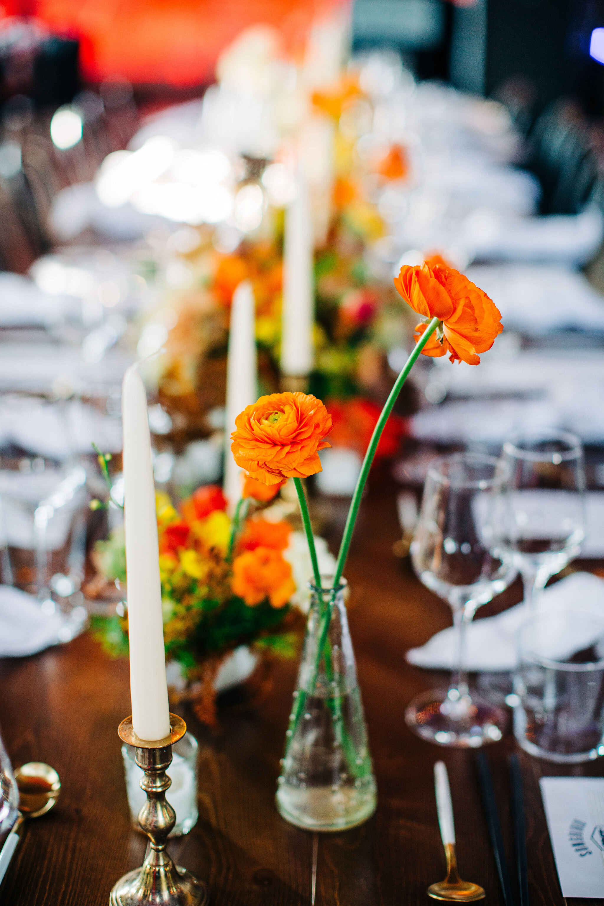 Yellow peonies, orange ranunculus, and golden fern floral centerpieces with brass candlesticks. Nashville wedding florist.