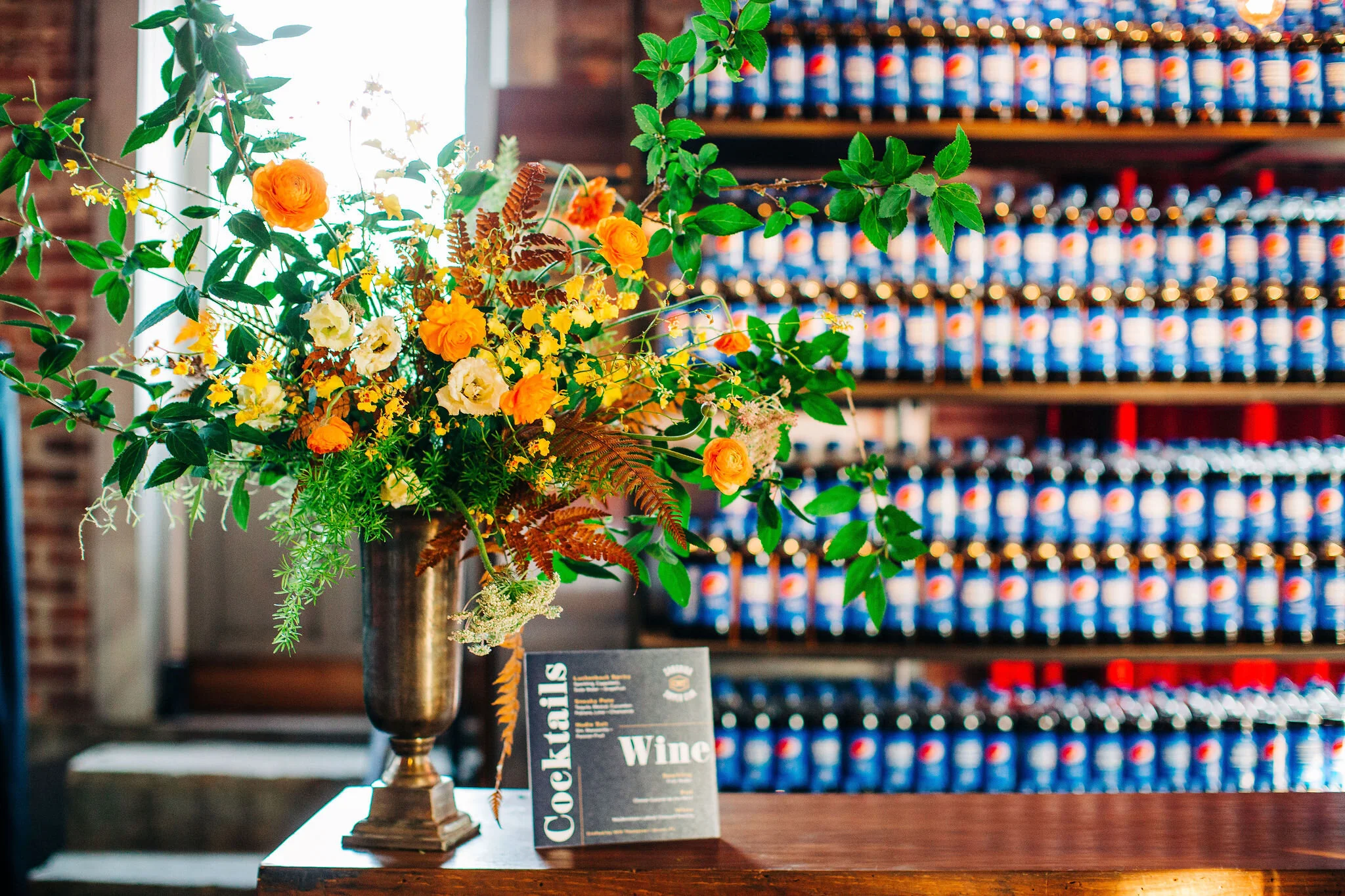 Yellow peonies, orange ranunculus, and golden fern floral centerpieces with brass candlesticks. Nashville wedding florist.