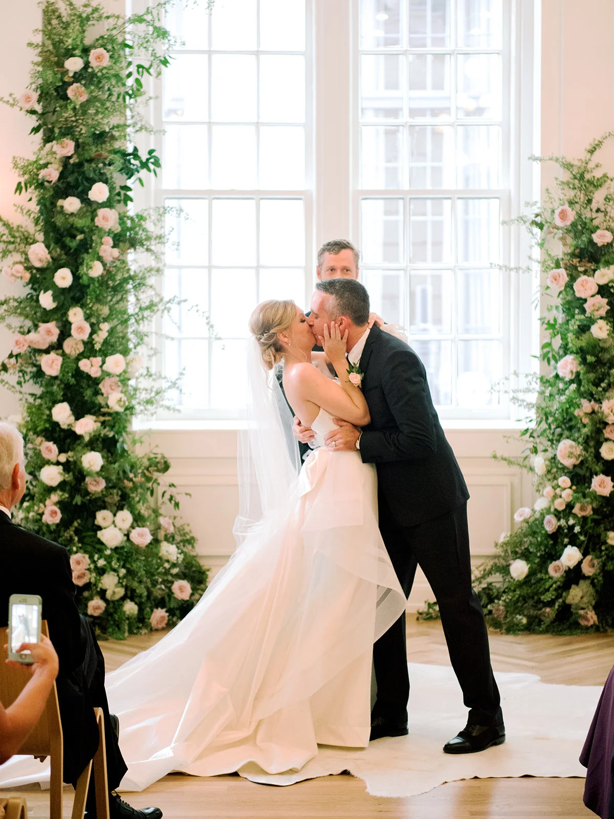 White wall venue with mid-century modern chandeliers and lush greenery floral installation for a Nashville wedding ceremony.