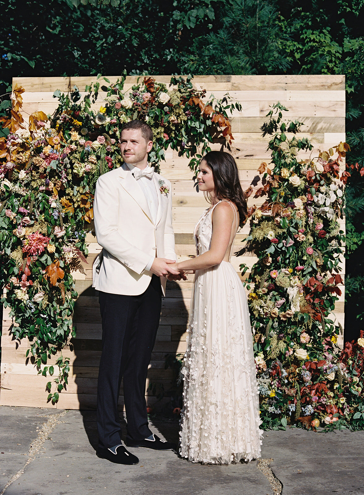 Reclaimed wood wall built by the father of the bride with lush, garden-inspired floral installation, using wildflowers, hops, fruiting branches, copper beech, ranunculus, garden roses, and tulips. RT Lodge wedding ceremony flowers.