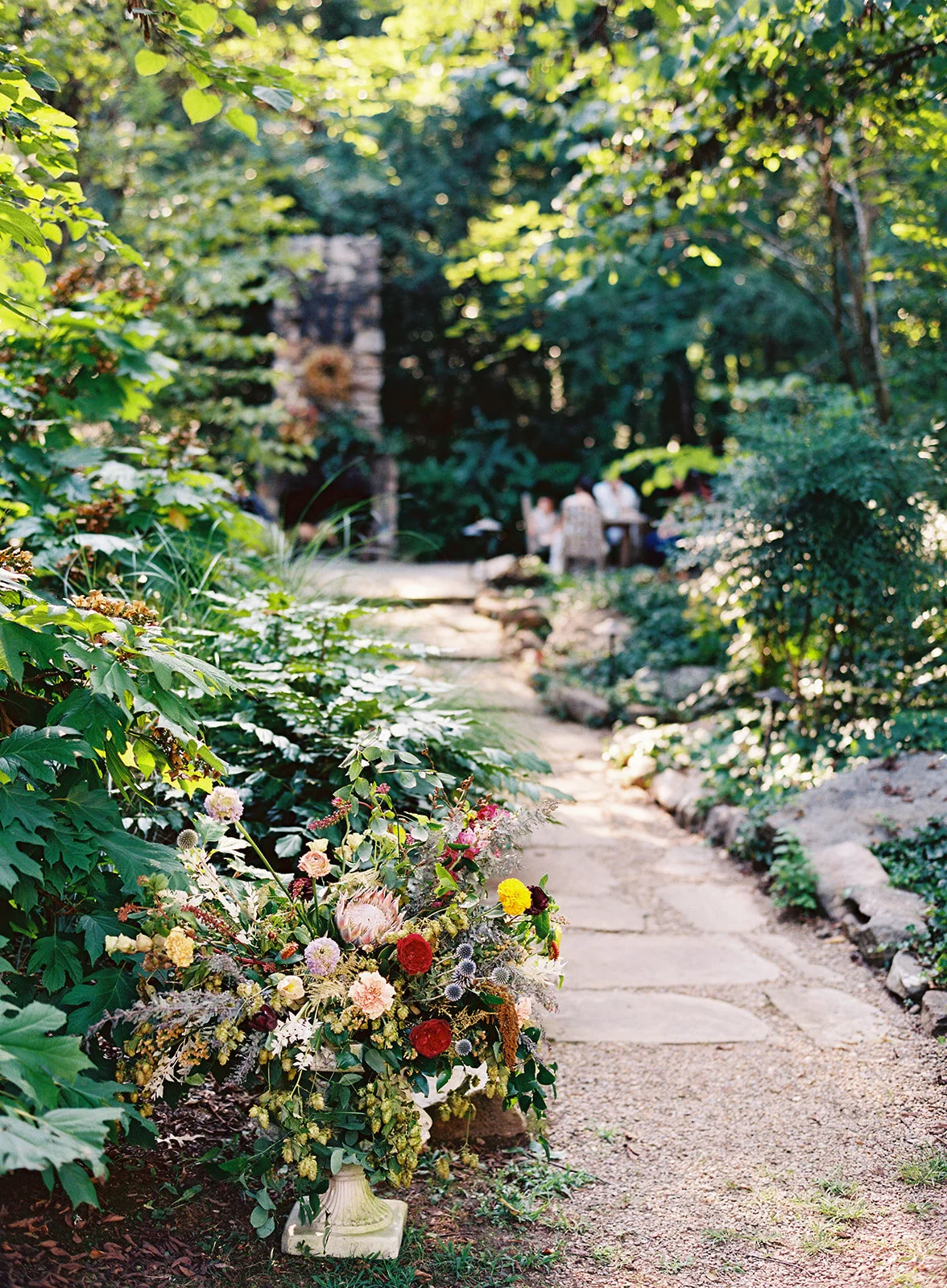 Large garden urn with an airy, natural flower arrangement of wildflowers in shades of coral, mauve, golden yellow, dusty blue, peach, and rosy pink. Nashville and Knoxville wedding floral designer at RT Lodge.