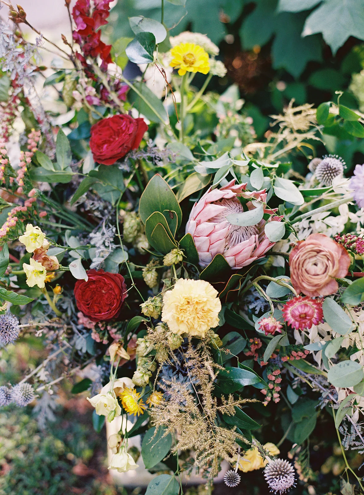 Large garden urn with an airy, natural flower arrangement of wildflowers in shades of coral, mauve, golden yellow, dusty blue, peach, and rosy pink. Nashville and Knoxville wedding floral designer at RT Lodge.