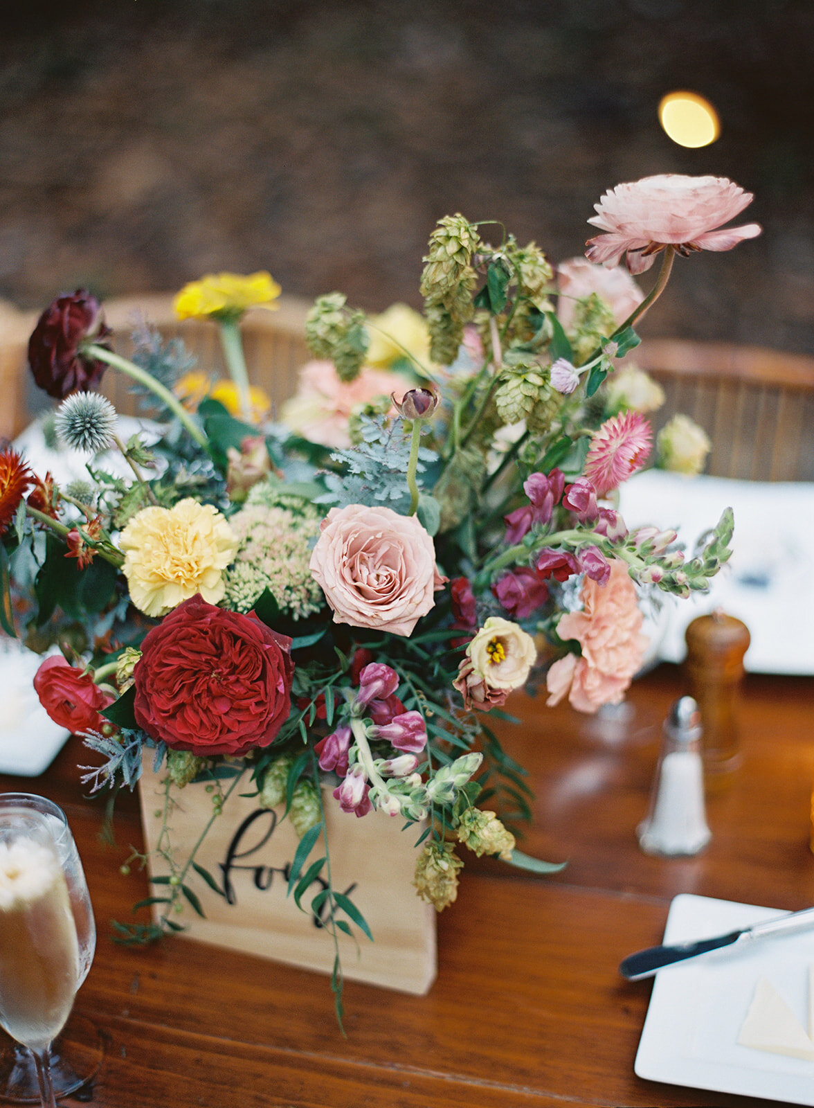 Garden urn wildflower centerpiece with deep red garden roses, dusty pink ranunculus, hops, berries, maroon snapdragon, thistles, golden yellow zinnias, and natural greenery. RT Lodge and Nashville luxury wedding floral designer.