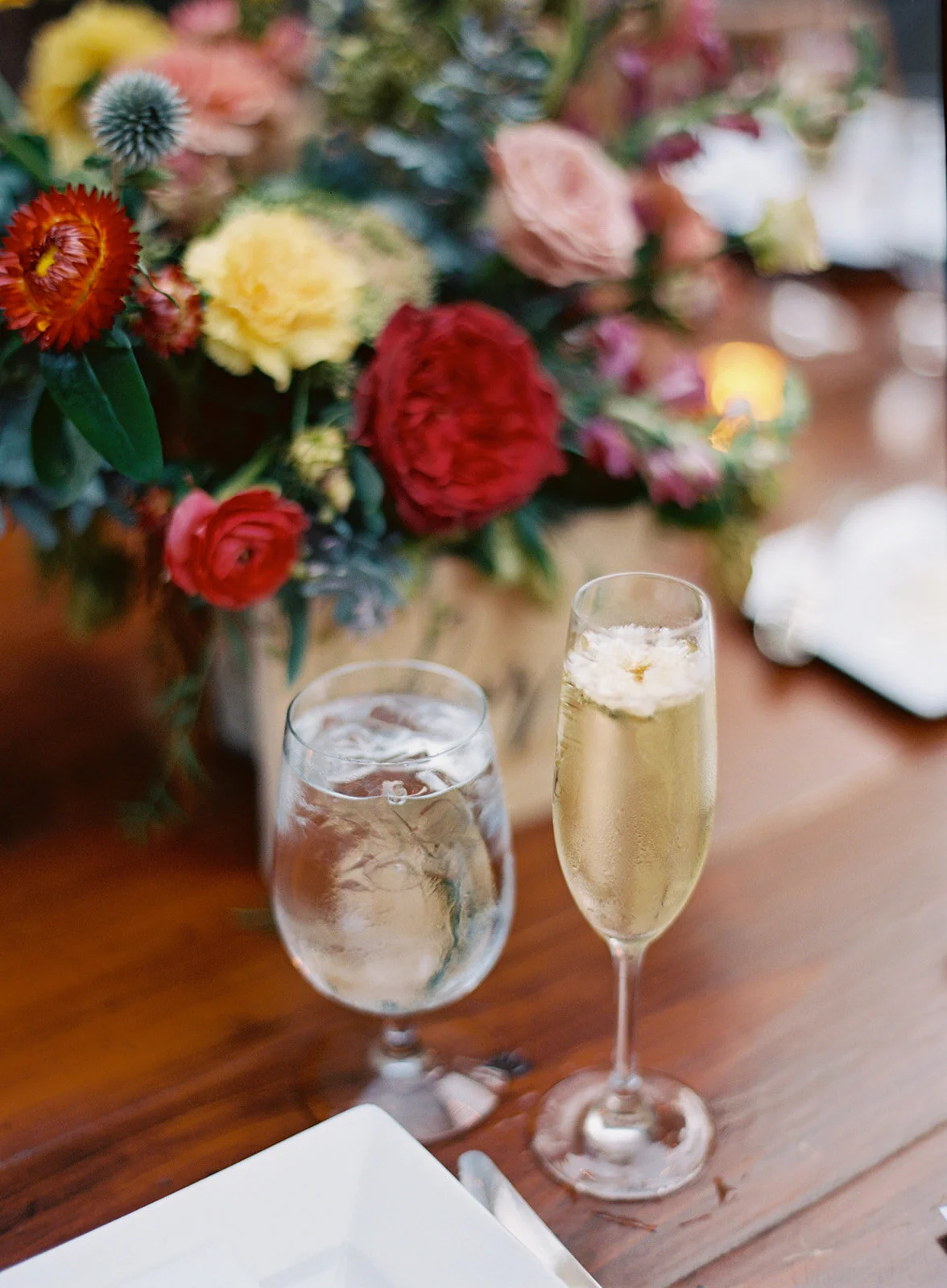 Garden urn wildflower centerpiece with deep red garden roses, dusty pink ranunculus, hops, berries, maroon snapdragon, thistles, golden yellow zinnias, and natural greenery. RT Lodge and Nashville luxury wedding floral designer.