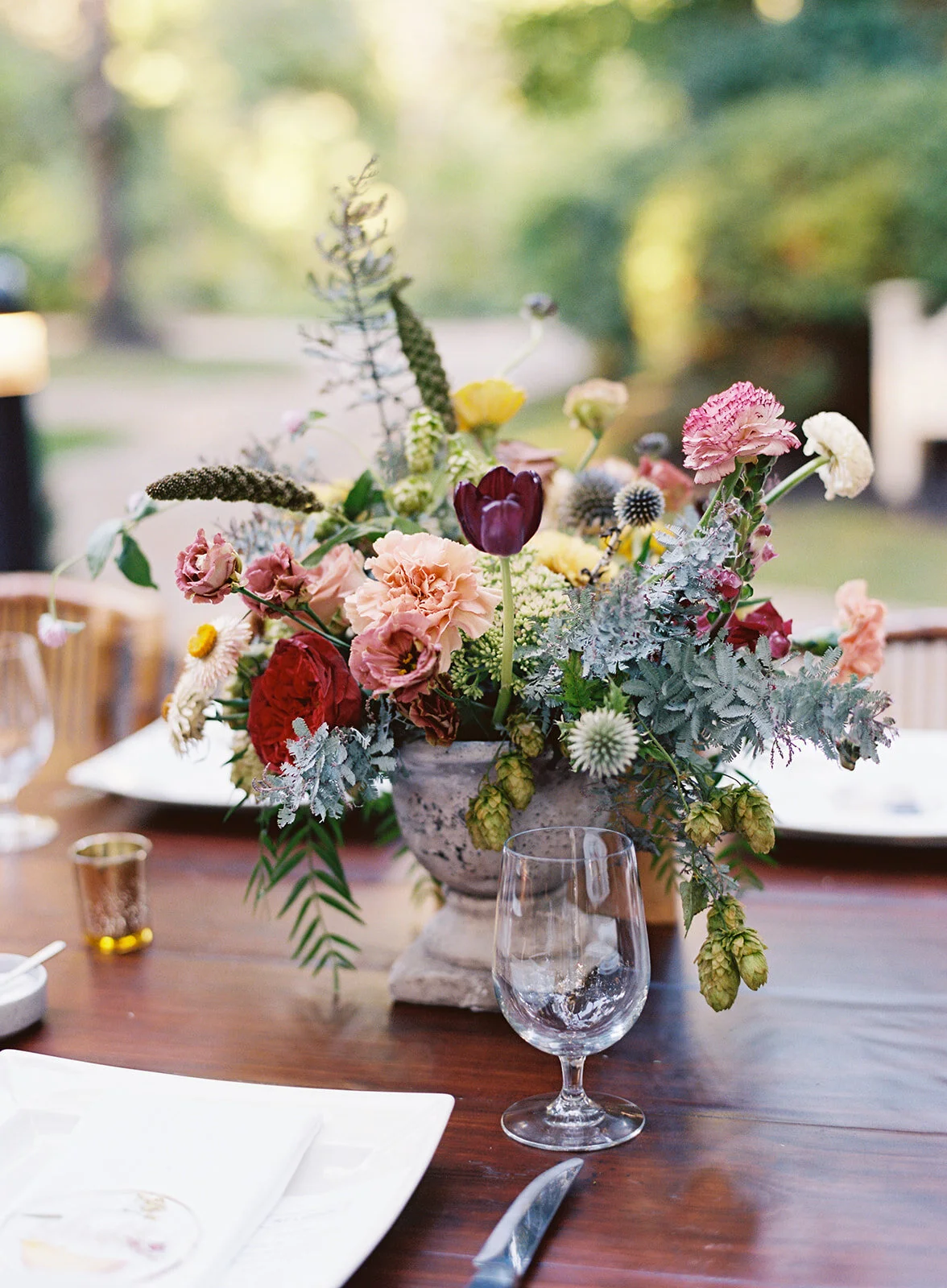 Garden urn wildflower centerpiece with deep red garden roses, dusty pink ranunculus, hops, berries, maroon snapdragon, thistles, golden yellow zinnias, and natural greenery. RT Lodge and Nashville luxury wedding floral designer.