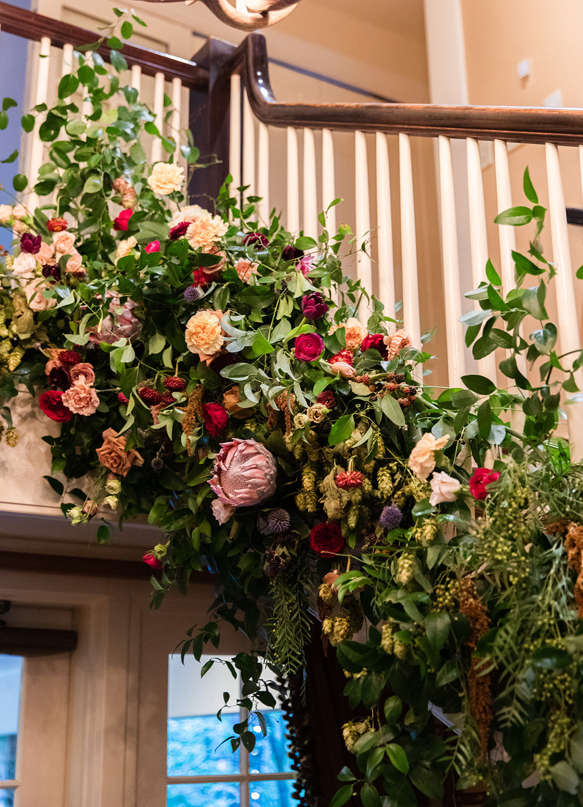 Early fall wedding floral design at RT Lodge. Lush, untamed installation growing up the staircase with wildflowers, protea, fruiting branches, ranunculus, garden roses, and dried textures.