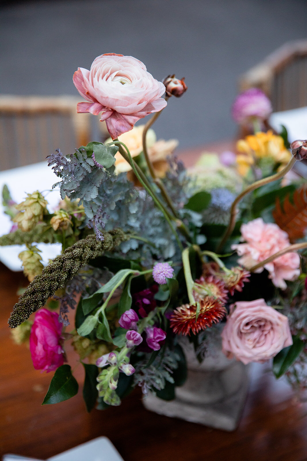 Garden urn wildflower centerpiece with deep red garden roses, dusty pink ranunculus, hops, berries, maroon snapdragon, thistles, golden yellow zinnias, and natural greenery. RT Lodge and Nashville luxury wedding floral designer.