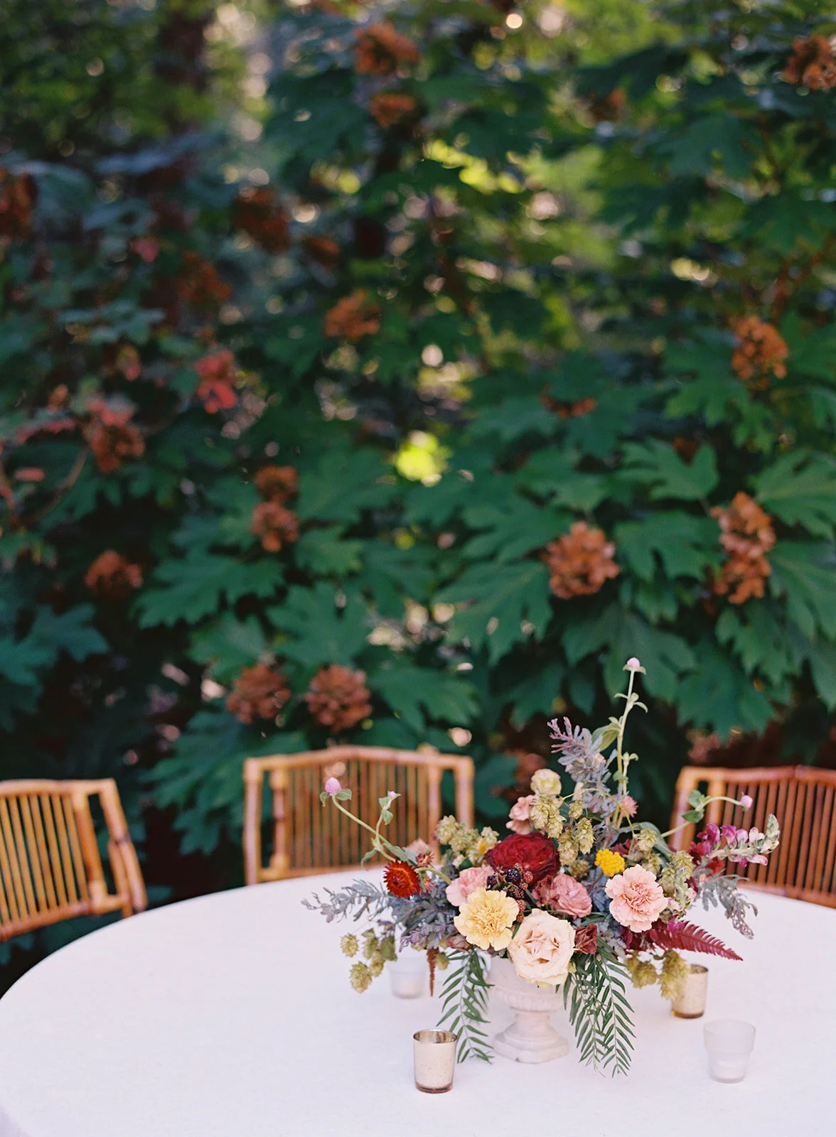 Garden urn wildflower centerpiece with deep red garden roses, dusty pink ranunculus, hops, berries, maroon snapdragon, thistles, golden yellow zinnias, and natural greenery. RT Lodge and Nashville luxury wedding floral designer.