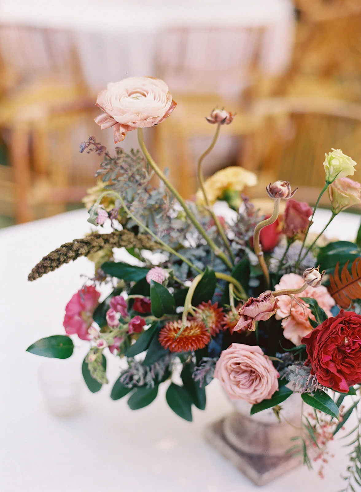Garden urn wildflower centerpiece with deep red garden roses, dusty pink ranunculus, hops, berries, maroon snapdragon, thistles, golden yellow zinnias, and natural greenery. RT Lodge and Nashville luxury wedding floral designer.