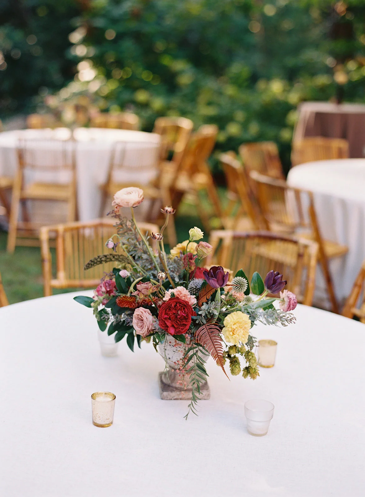 Garden urn wildflower centerpiece with deep red garden roses, dusty pink ranunculus, hops, berries, maroon snapdragon, thistles, golden yellow zinnias, and natural greenery. RT Lodge and Nashville luxury wedding floral designer.