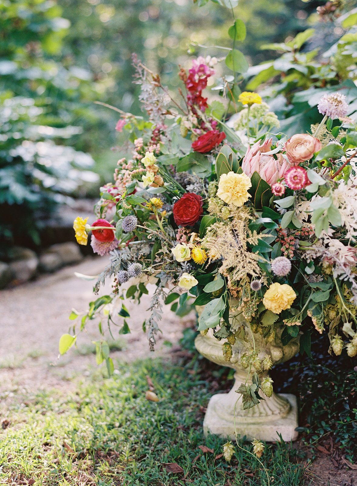 Large garden urn with an airy, natural flower arrangement of wildflowers in shades of coral, mauve, golden yellow, dusty blue, peach, and rosy pink. Nashville and Knoxville wedding floral designer at RT Lodge.