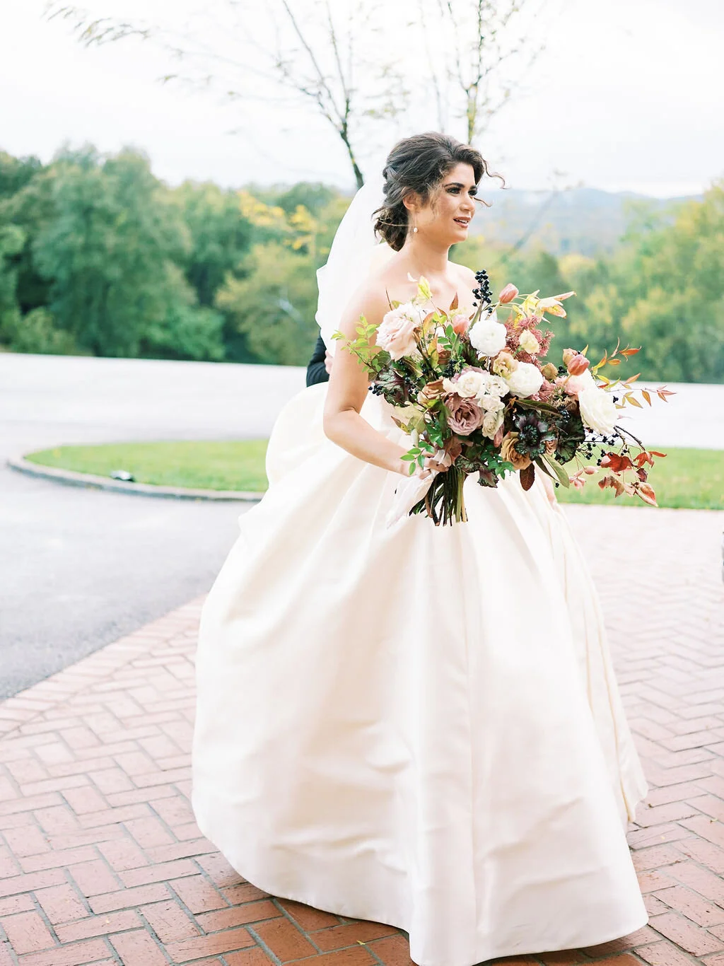 Lush, wild, untamed fall bridal bouquet with a muted autumnal color palette, composed of ligustrum berries, dusty pink ranunculus, tulips, garden roses, fall leaves, begonia leaves, and muted textures. Nashville wedding and corporate event floral de…