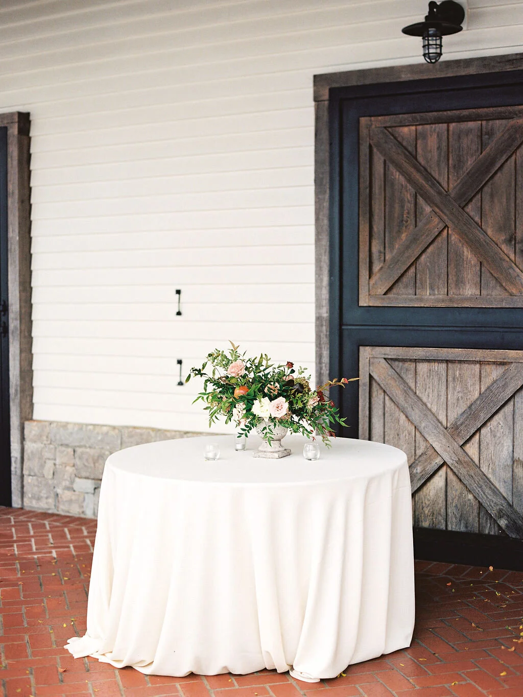Low European garden urn overflowing with a natural floral arrangement of garden roses, ranunculus, festival bush, fruiting persimmon branches, organic greenery, and fall berries. Centerpiece for a Trinity View Farm wedding by Nashville florist, Rose…