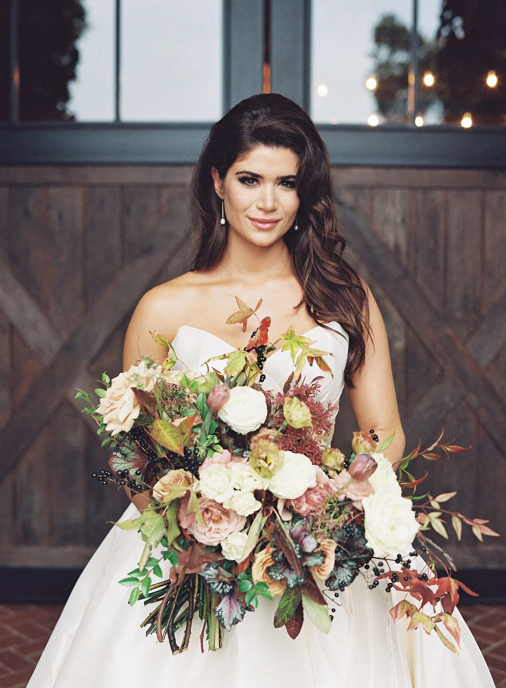Lush, wild, untamed fall bridal bouquet with a muted autumnal color palette, composed of ligustrum berries, dusty pink ranunculus, tulips, garden roses, fall leaves, begonia leaves, and muted textures. Nashville wedding and corporate event floral de…