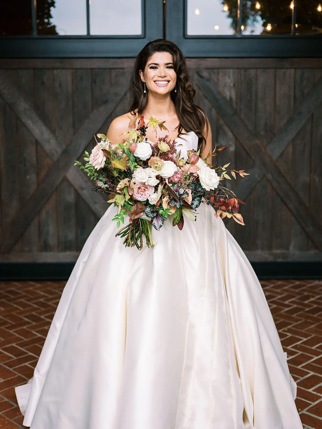 Lush, wild, untamed fall bridal bouquet with a muted autumnal color palette, composed of ligustrum berries, dusty pink ranunculus, tulips, garden roses, fall leaves, begonia leaves, and muted textures. Nashville wedding and corporate event floral de…