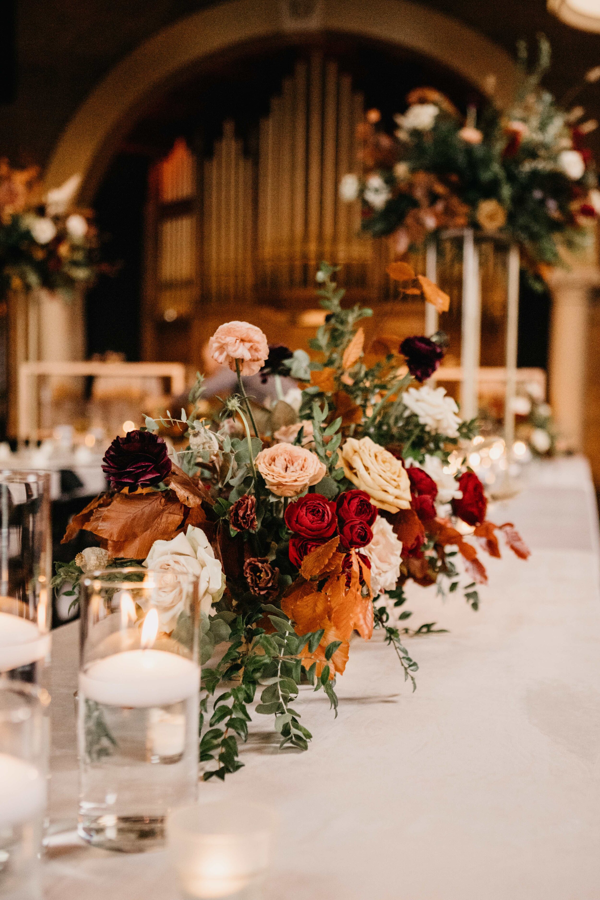 Modern gold stands with lush, asymmetrical floral arrangements using copper beech, pampas grass, garden roses, dahlias, and ranunculus in shades on rusty orange, burgundy, and muted earth tones. Nashville wedding floral design at Clementine.