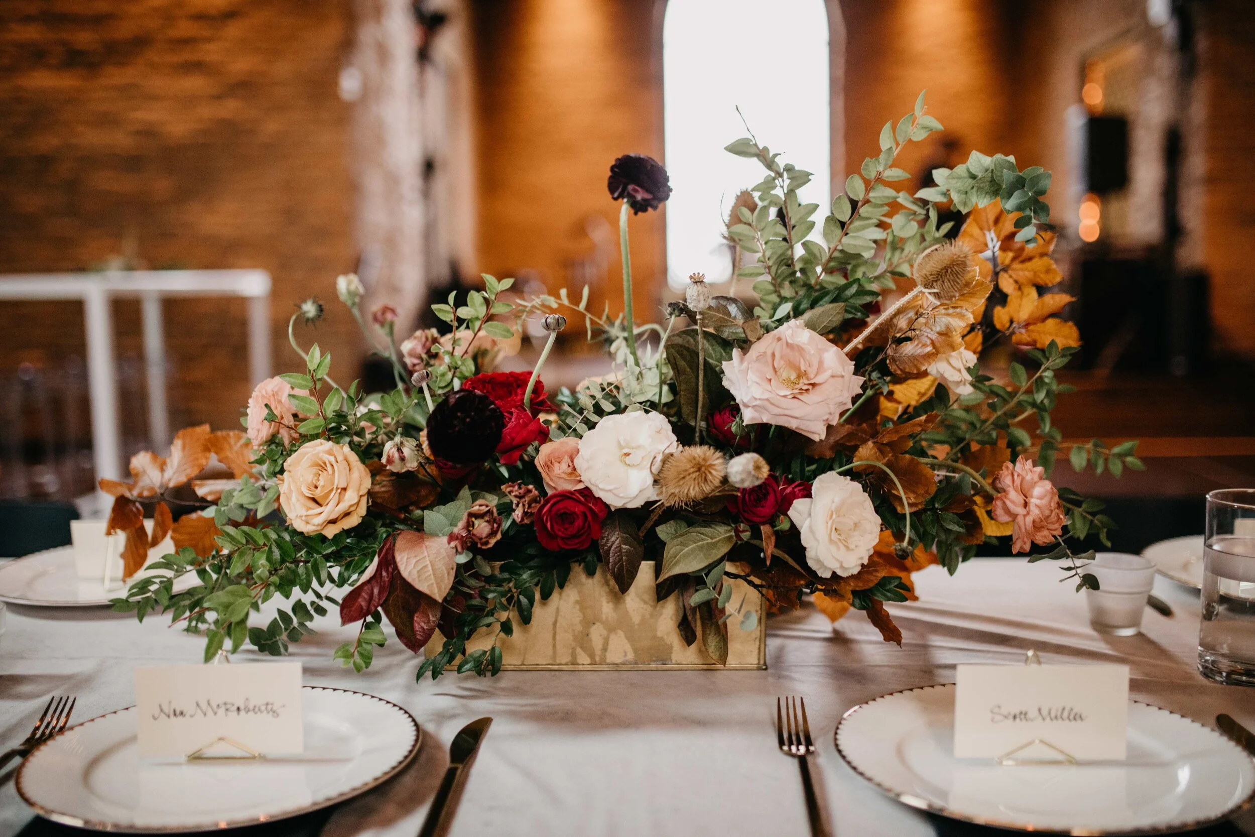 Low gold metal vessel for autumnal, textured floral centerpiece with greenery, garden roses, ranunculus, and fall foliage. Nashville, TN and Southeastern US luxury floral designer, Rosemary & Finch.