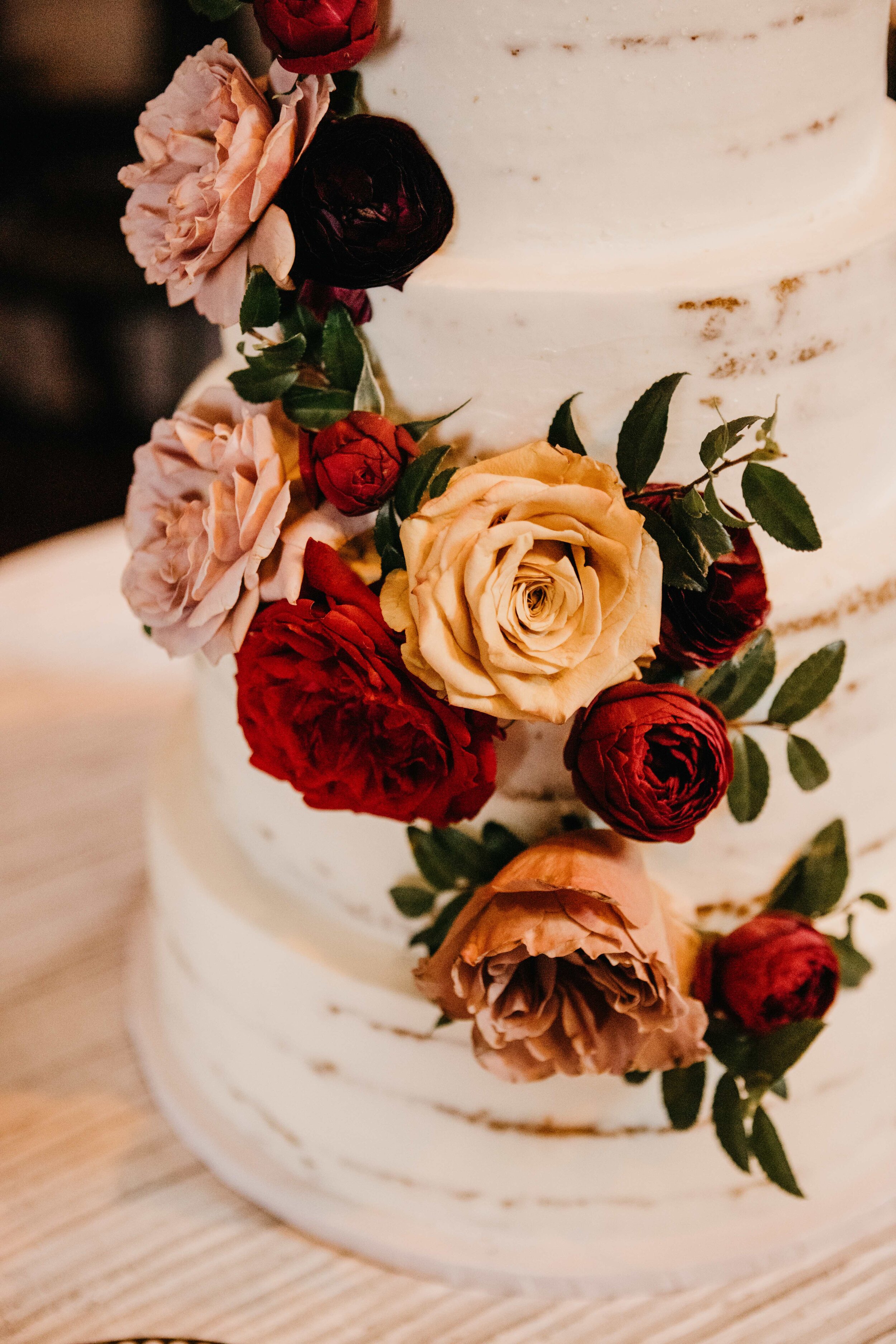 Naked cake with full floral cascade of garden roses in shades of burgundy, golden yellow, and dusty rose pink. Nashville, TN luxury wedding floral design by Rosemary & Finch.