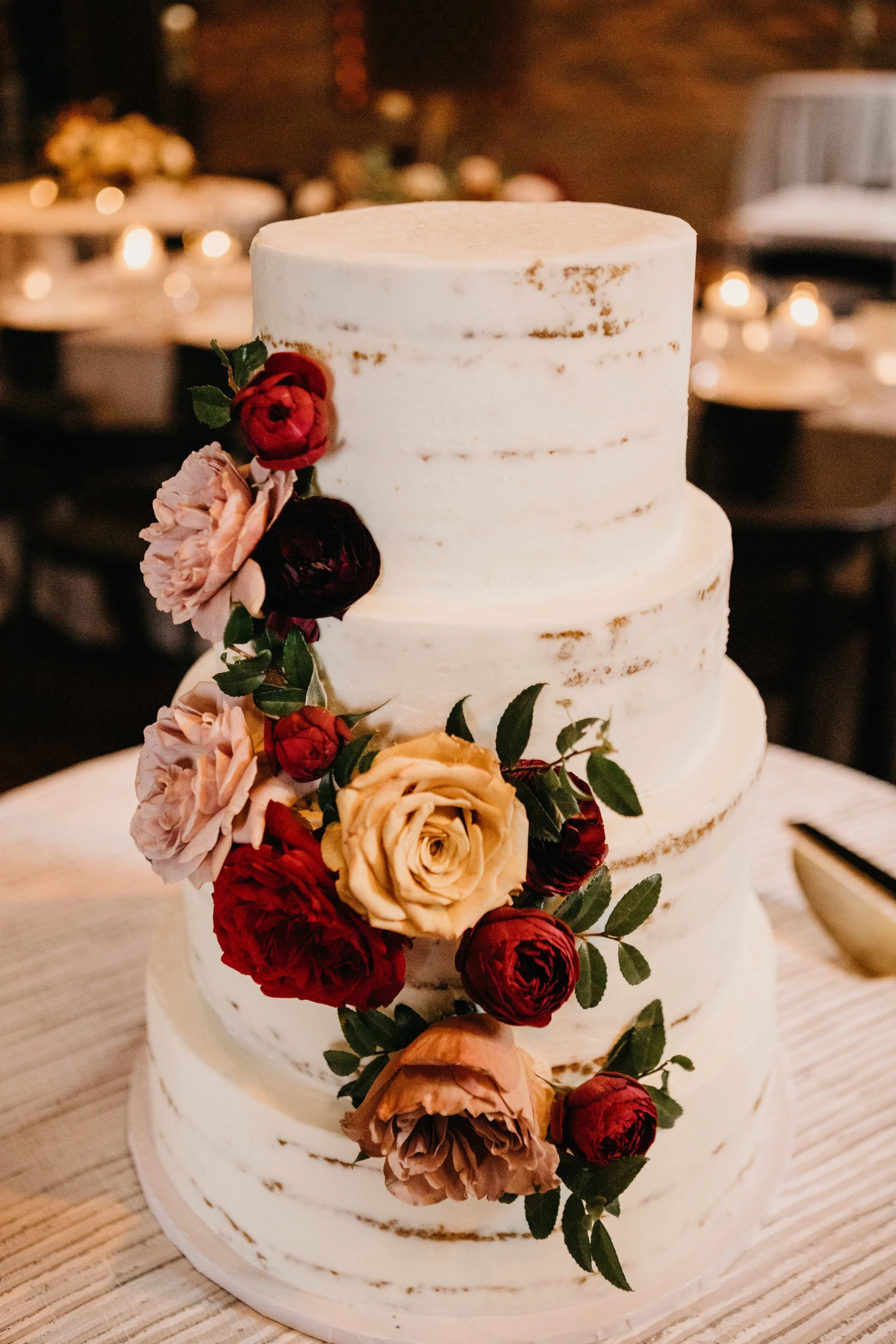 Naked cake with full floral cascade of garden roses in shades of burgundy, golden yellow, and dusty rose pink. Nashville, TN luxury wedding floral design by Rosemary & Finch.
