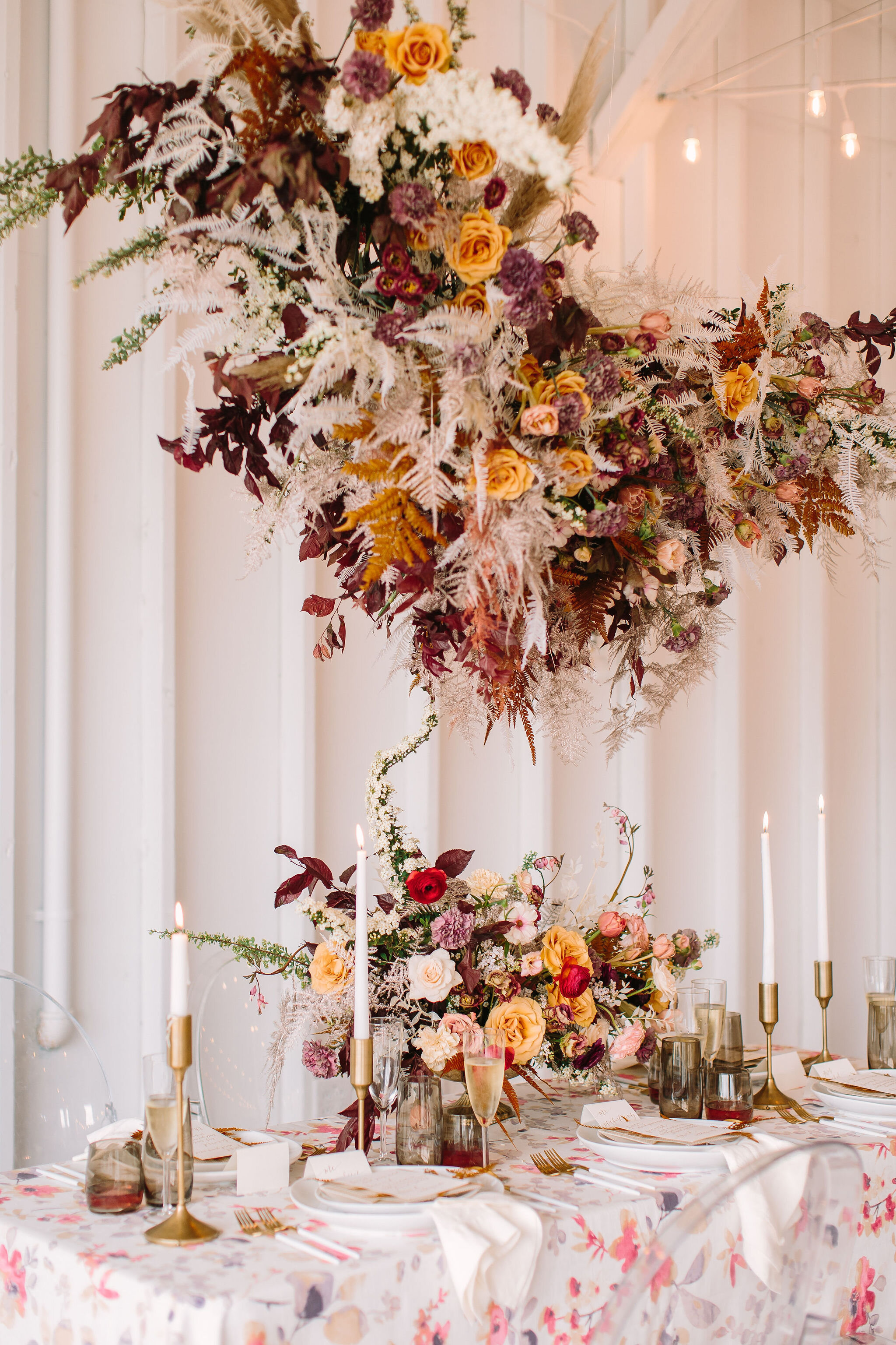 Modern hanging floral cloud installation with spirea, pampas grass, dried white fern, dyed plumosa, gold combo roses, Roseanne lisianthks, plum foliage, brown tulips, and red ranunculus. Nashville wedding and event floral design.