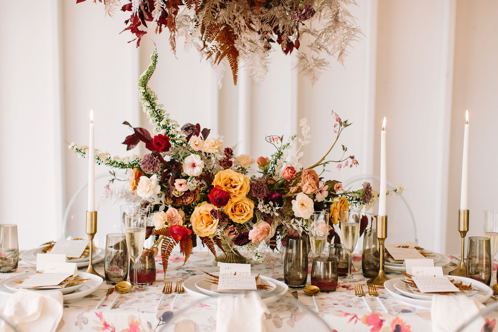 Low gold compote centerpiece with asymmetrical, natural flowers. Golden garden roses, deep red ranunculus, blush butterfly ranunculus, gold ferns, nine bark, dusty pink tulips, and spring wildflowers. Nashville wedding florist.