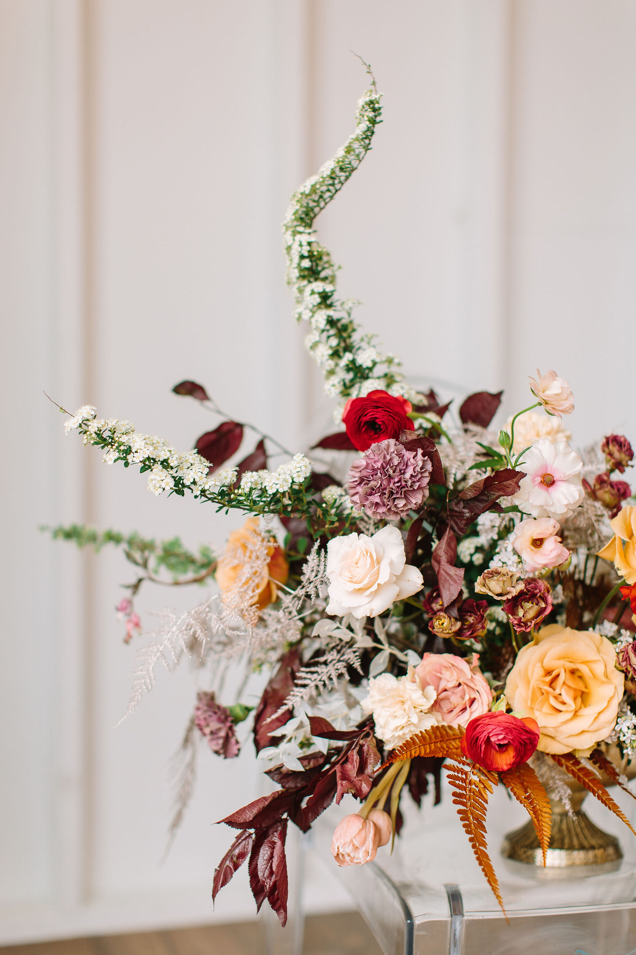Low gold compote centerpiece with asymmetrical, natural flowers. Golden garden roses, deep red ranunculus, blush butterfly ranunculus, gold ferns, nine bark, dusty pink tulips, and spring wildflowers. Nashville wedding florist.