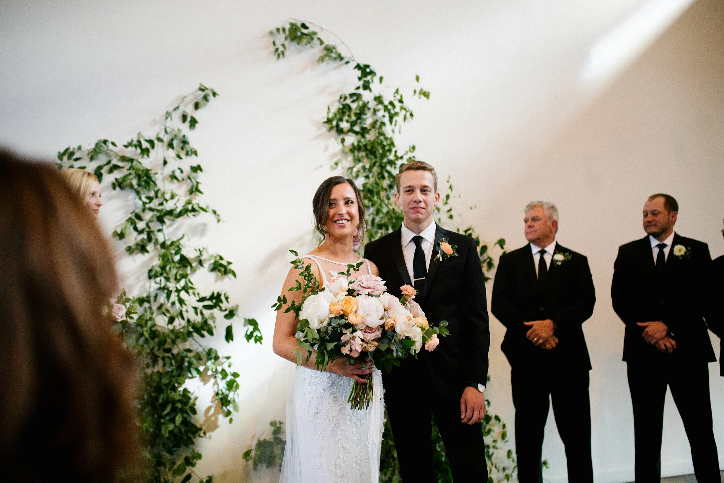 Vine-like greenery installation - creating an arch on the white wall at the Cordelle as the wedding ceremony backdrop. Nashville wedding floral design.