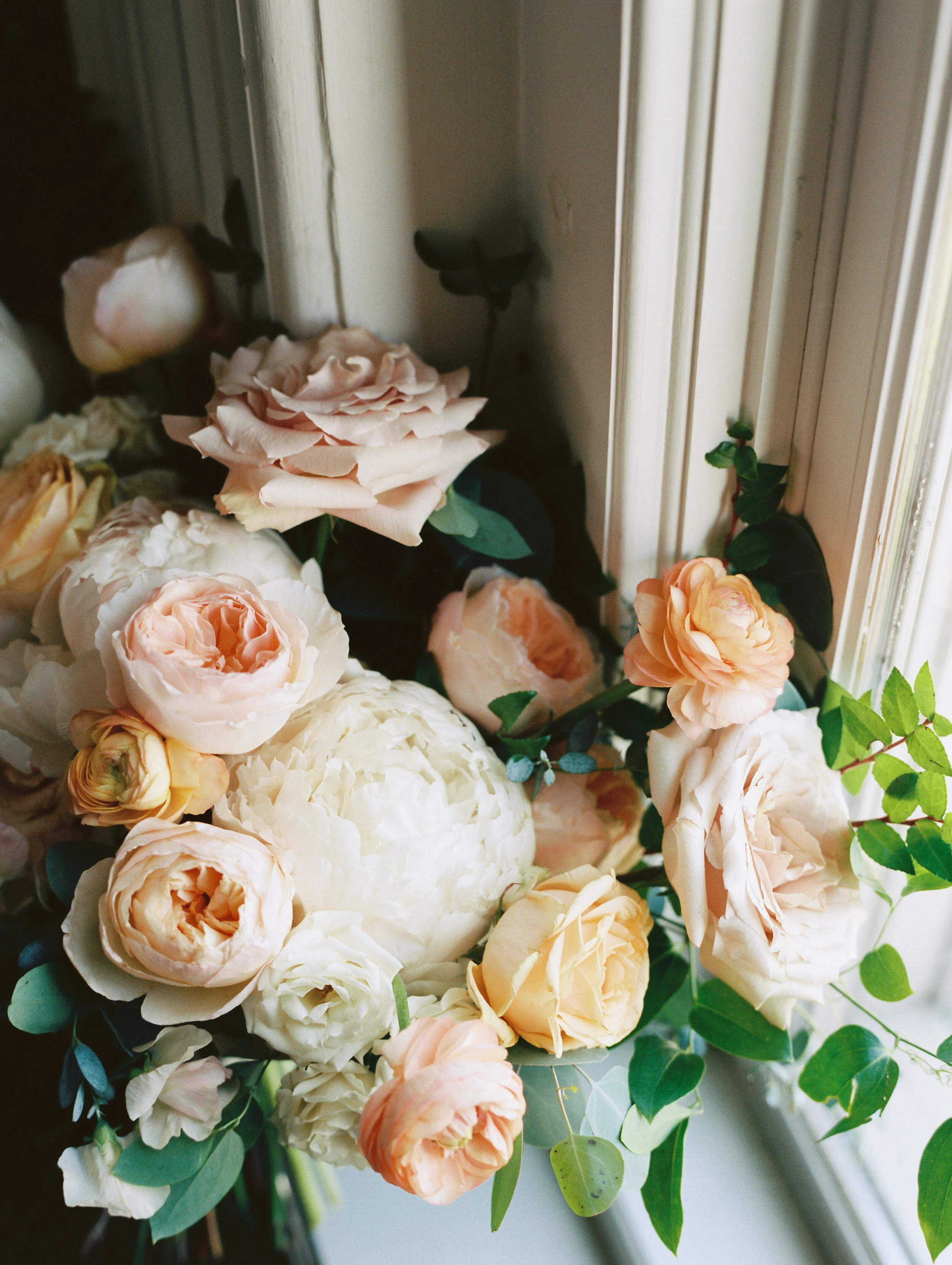 Bridal bouquet with peach ranunculus, cream peonies, blush and golden yellow garden roses, and natural, untamed greenery. June wedding at the Cordelle. Nashville Wedding Florist.