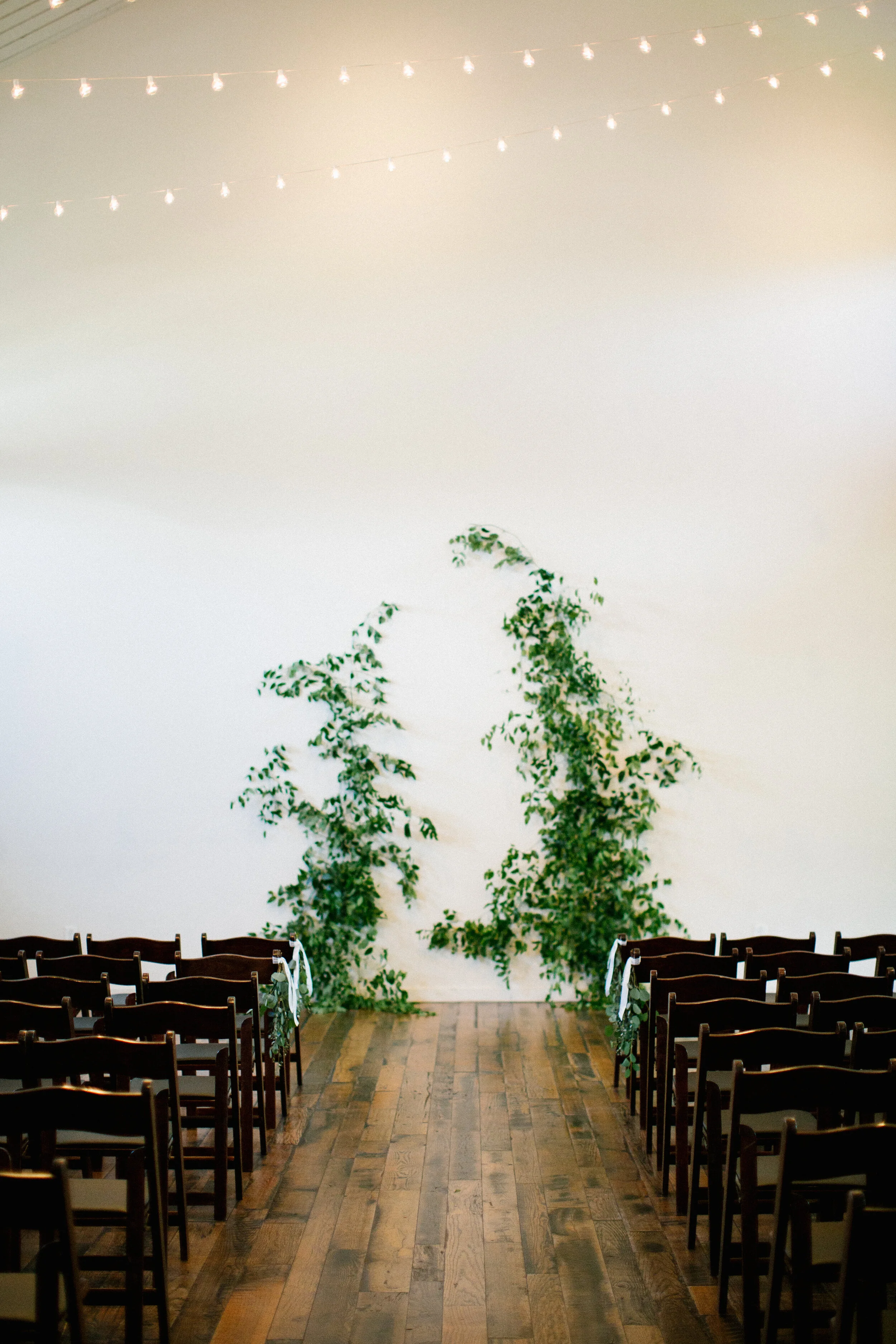 Vine-like greenery installation - creating an arch on the white wall at the Cordelle as the wedding ceremony backdrop. Nashville wedding floral design.