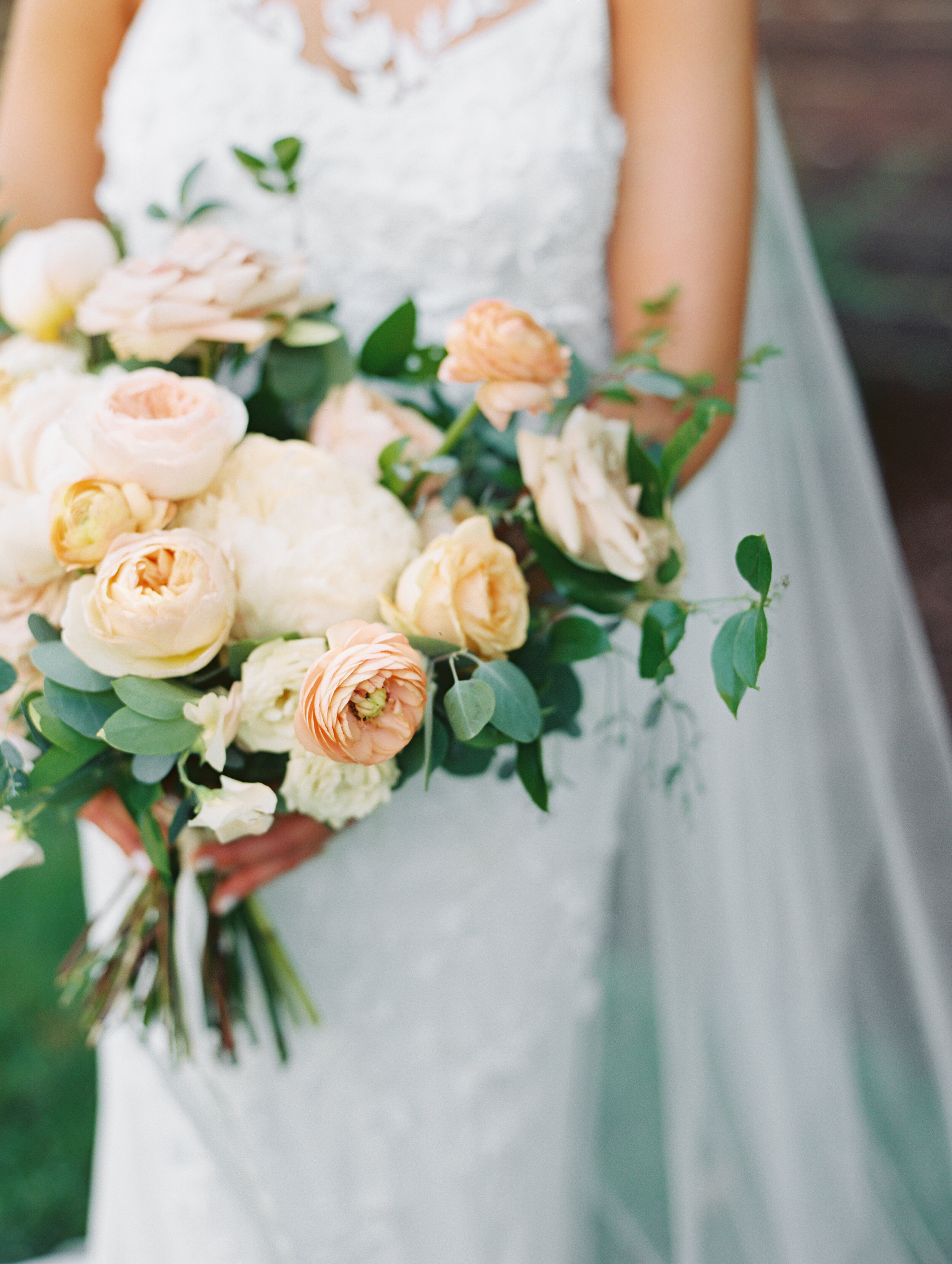 Bridal bouquet with peach ranunculus, cream peonies, blush and golden yellow garden roses, and natural, untamed greenery. June wedding at the Cordelle. Nashville Wedding Florist.