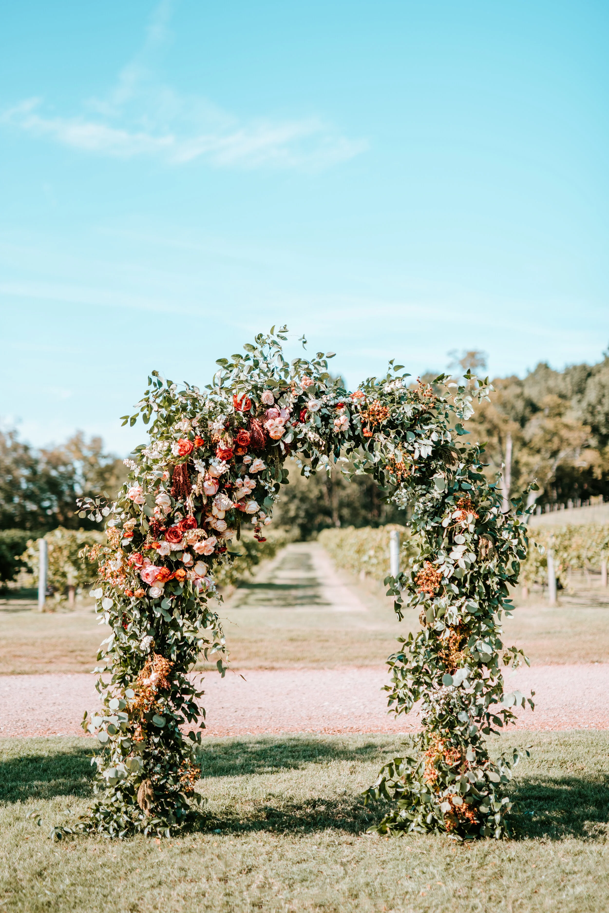 Lush floral arch for a fall wedding at Long Hollow Gardens with untamed greenery, berries, and rust orange garden roses.