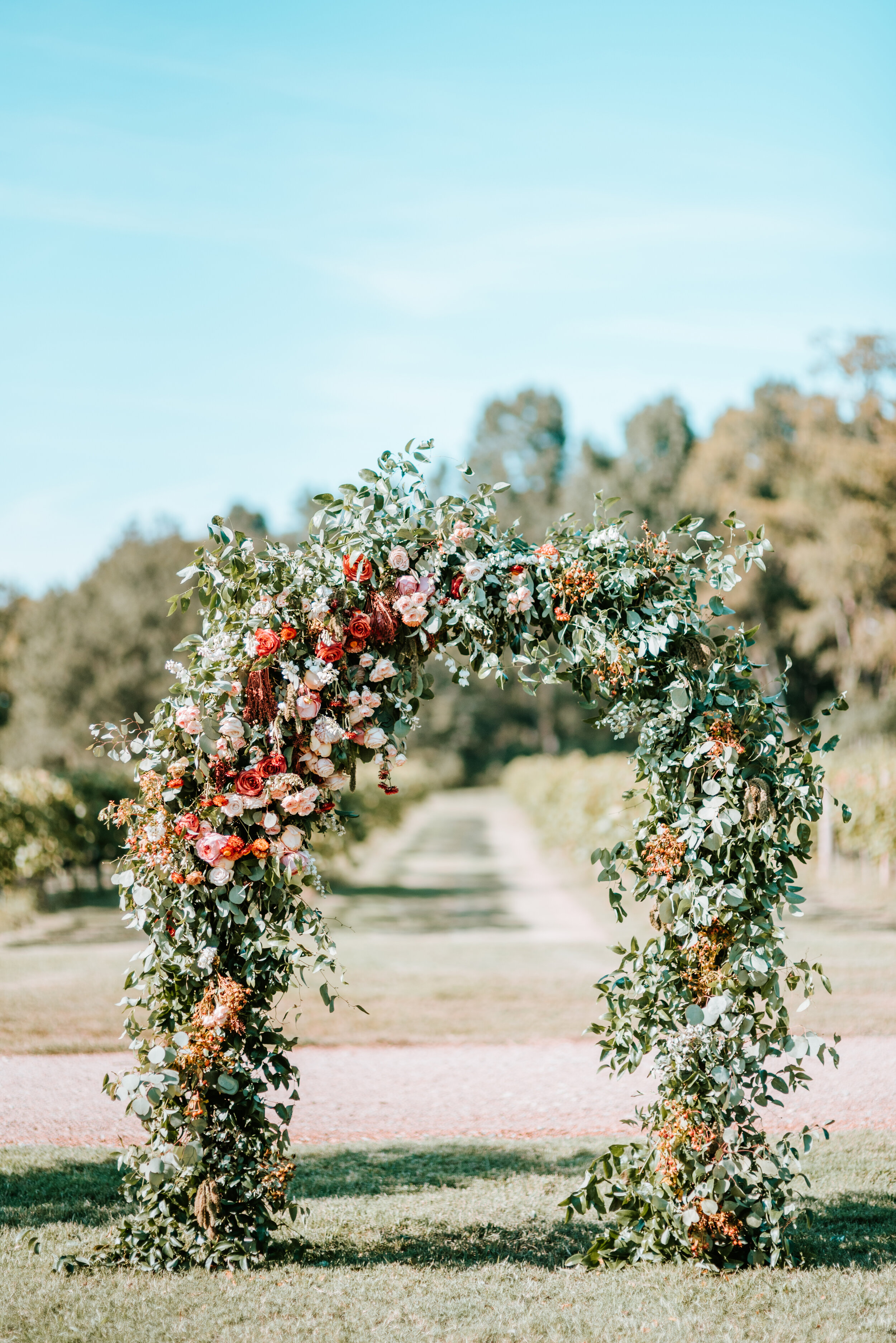Lush floral arch for a fall wedding at Long Hollow Gardens with untamed greenery, berries, and rust orange garden roses.