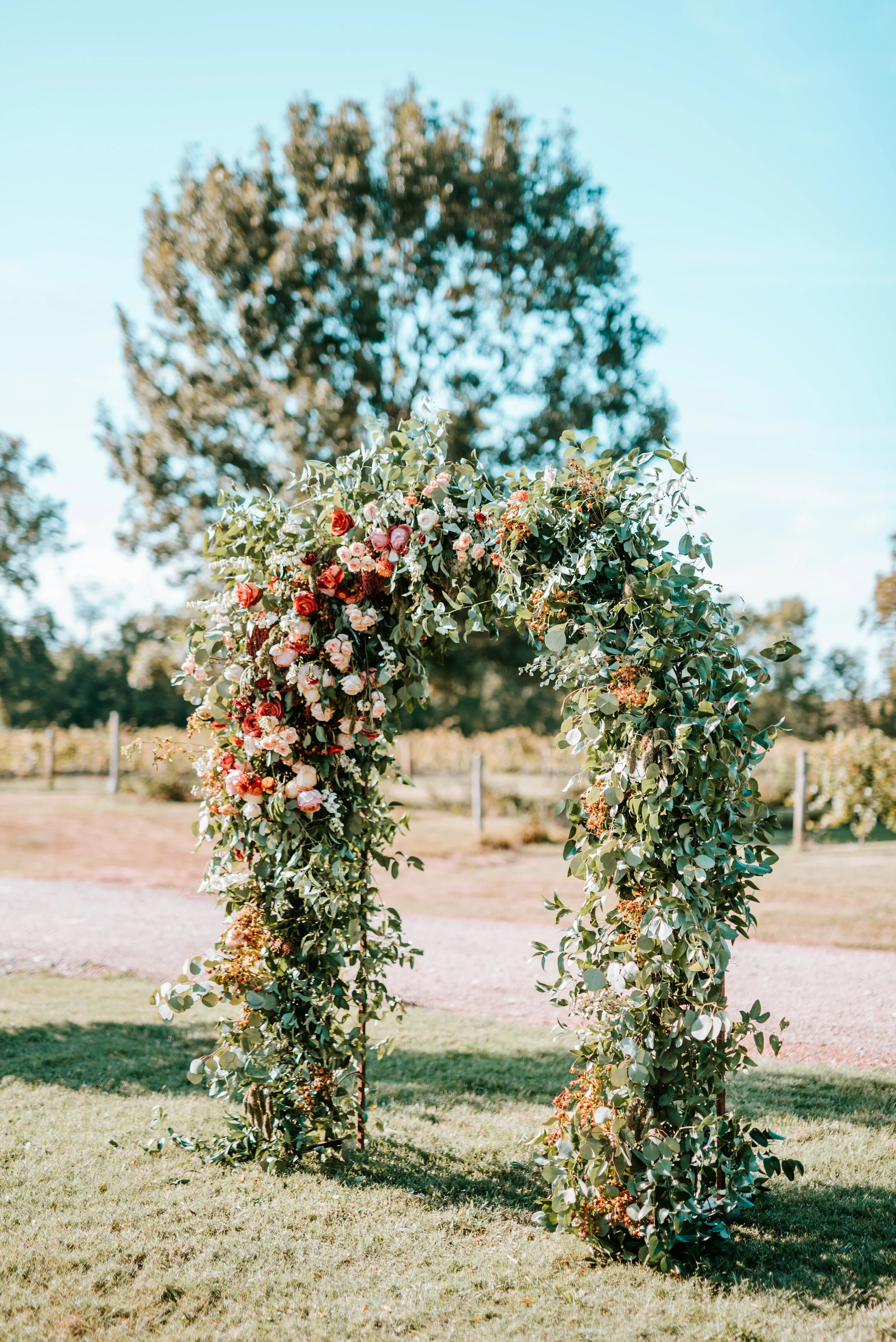 Lush floral arch for a fall wedding at Long Hollow Gardens with untamed greenery, berries, and rust orange garden roses.